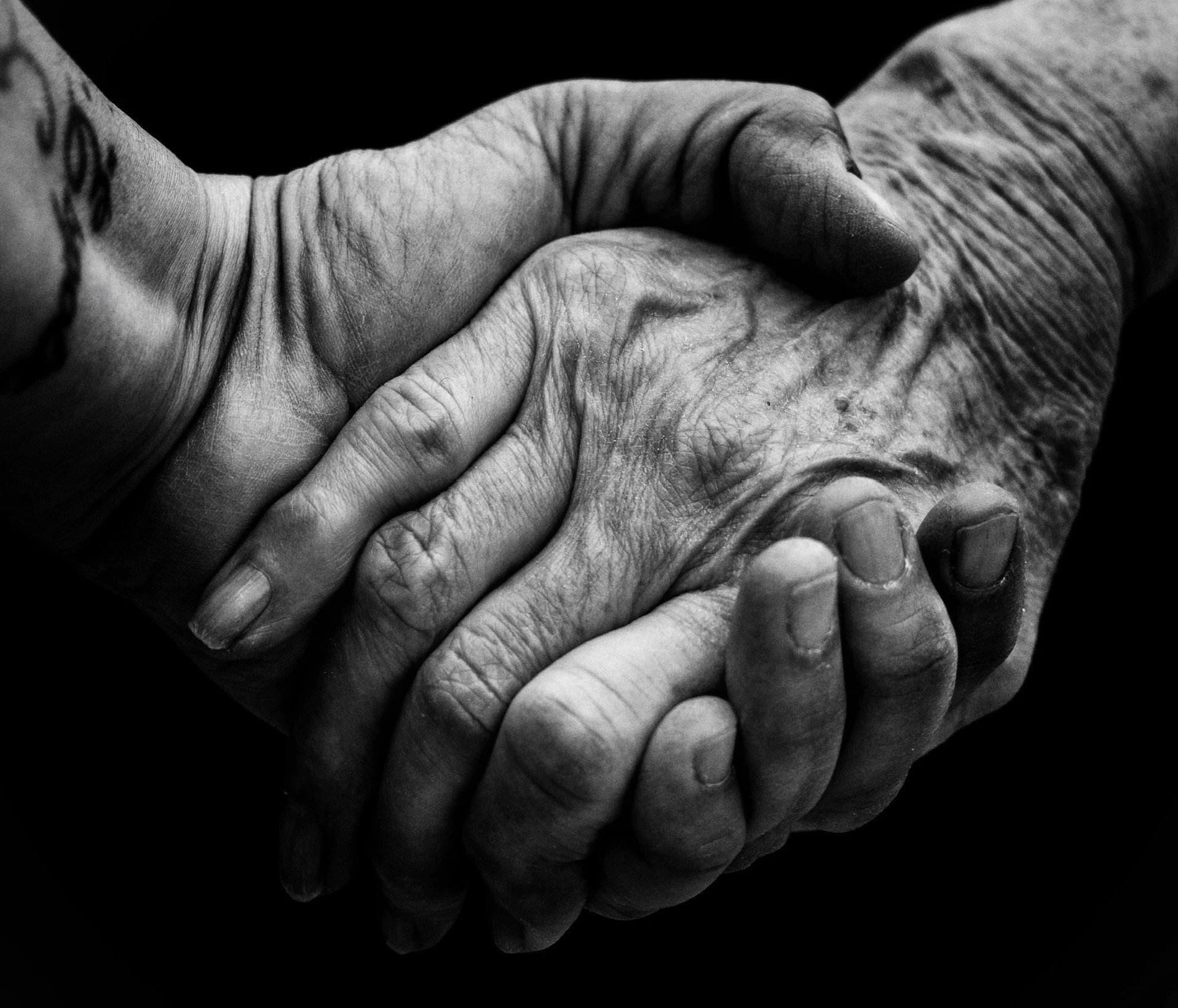Close-up of two hands holding each other, showing aged and wrinkled skin, signifying comfort and connection.