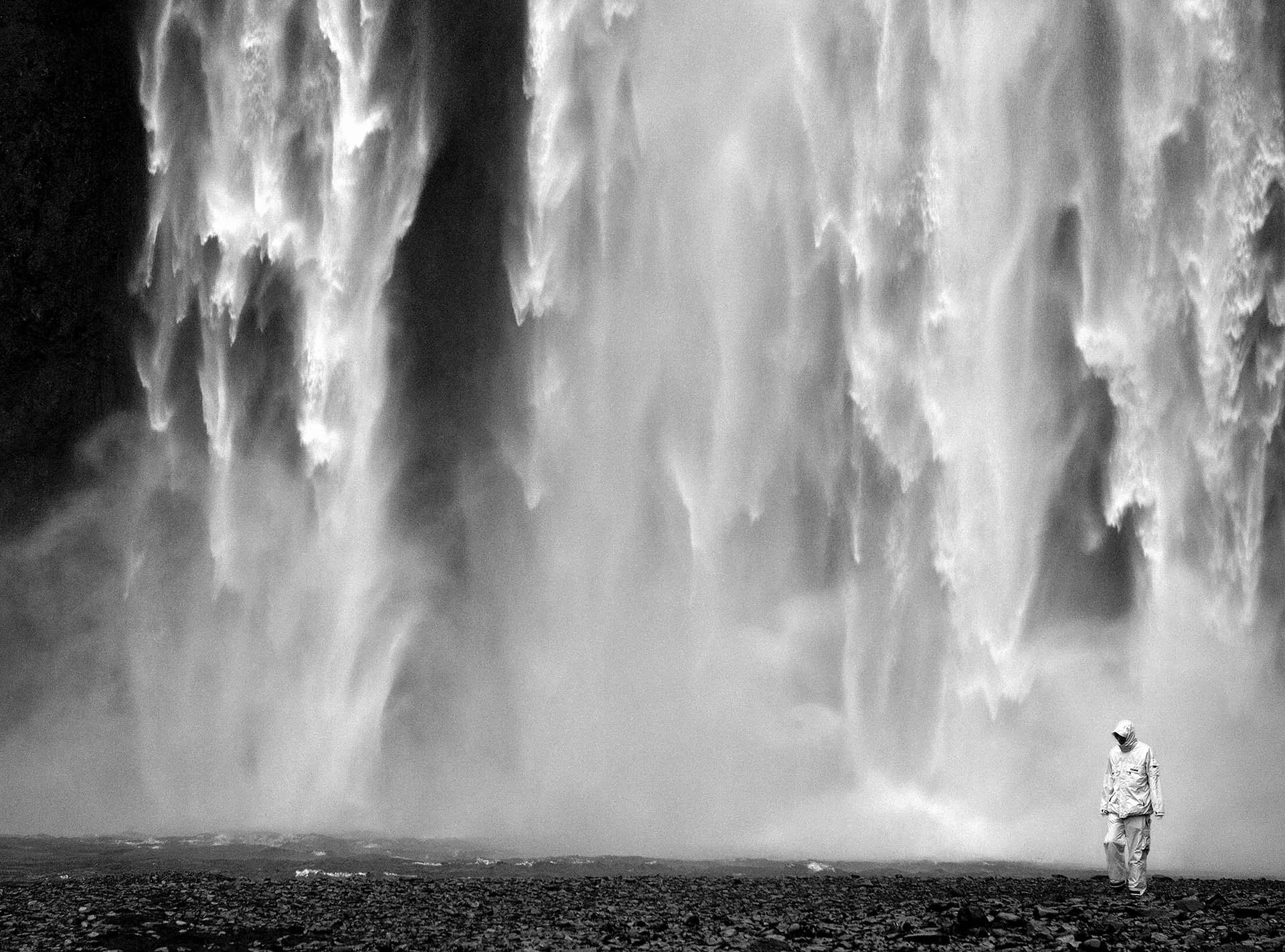 Person standing near a large waterfall in black and white