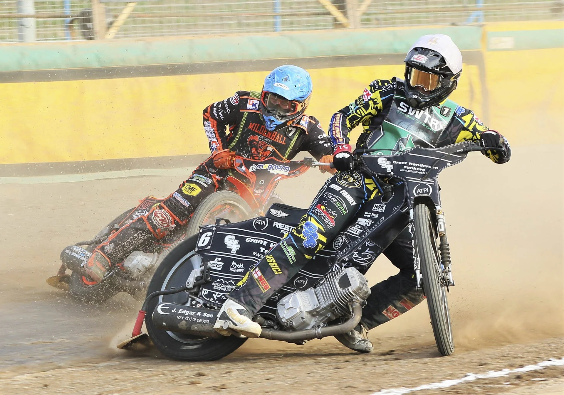 Two speedway motorcycle racers competing on a dirt track, wearing protective gear and helmets, creating dust trails behind them.