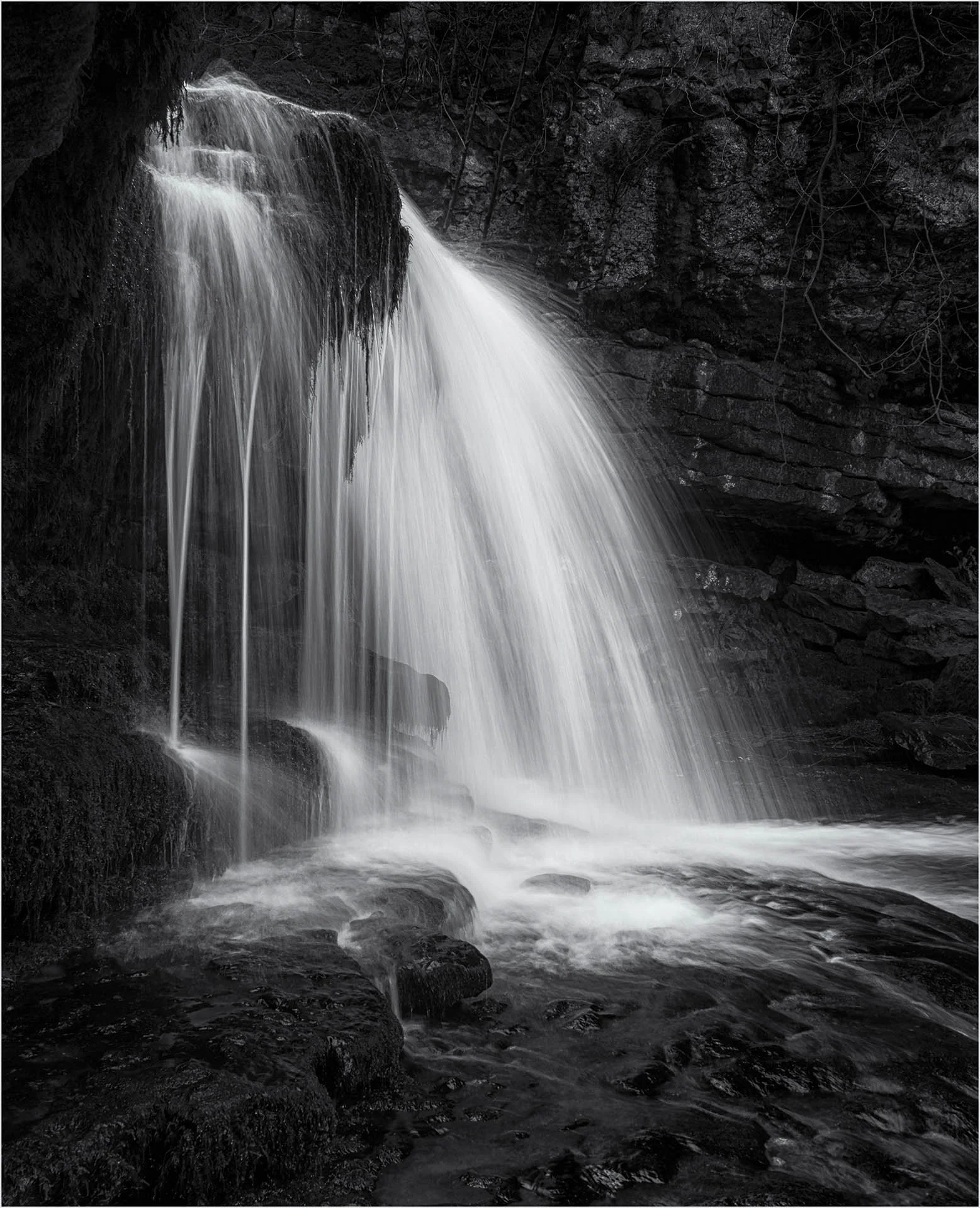 Black and white photograph of a waterfall cascading over rocks in a natural setting.