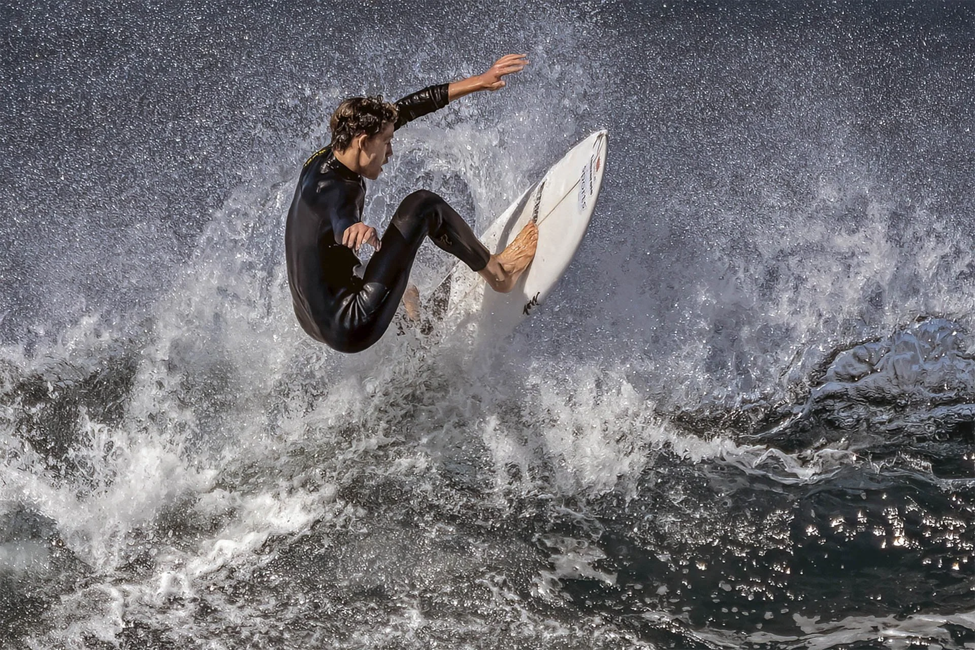 Surfer in black wetsuit performing maneuver on wave