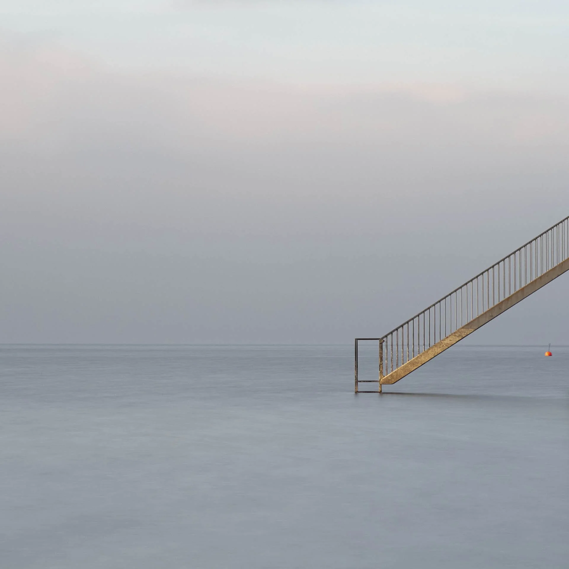Minimalist image of a metal staircase descending into calm water with a horizon in the background.