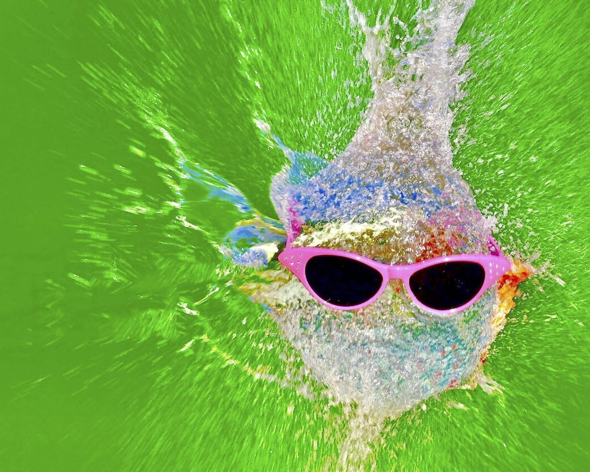 Pink sunglasses on a water balloon mid-explosion against a green background.