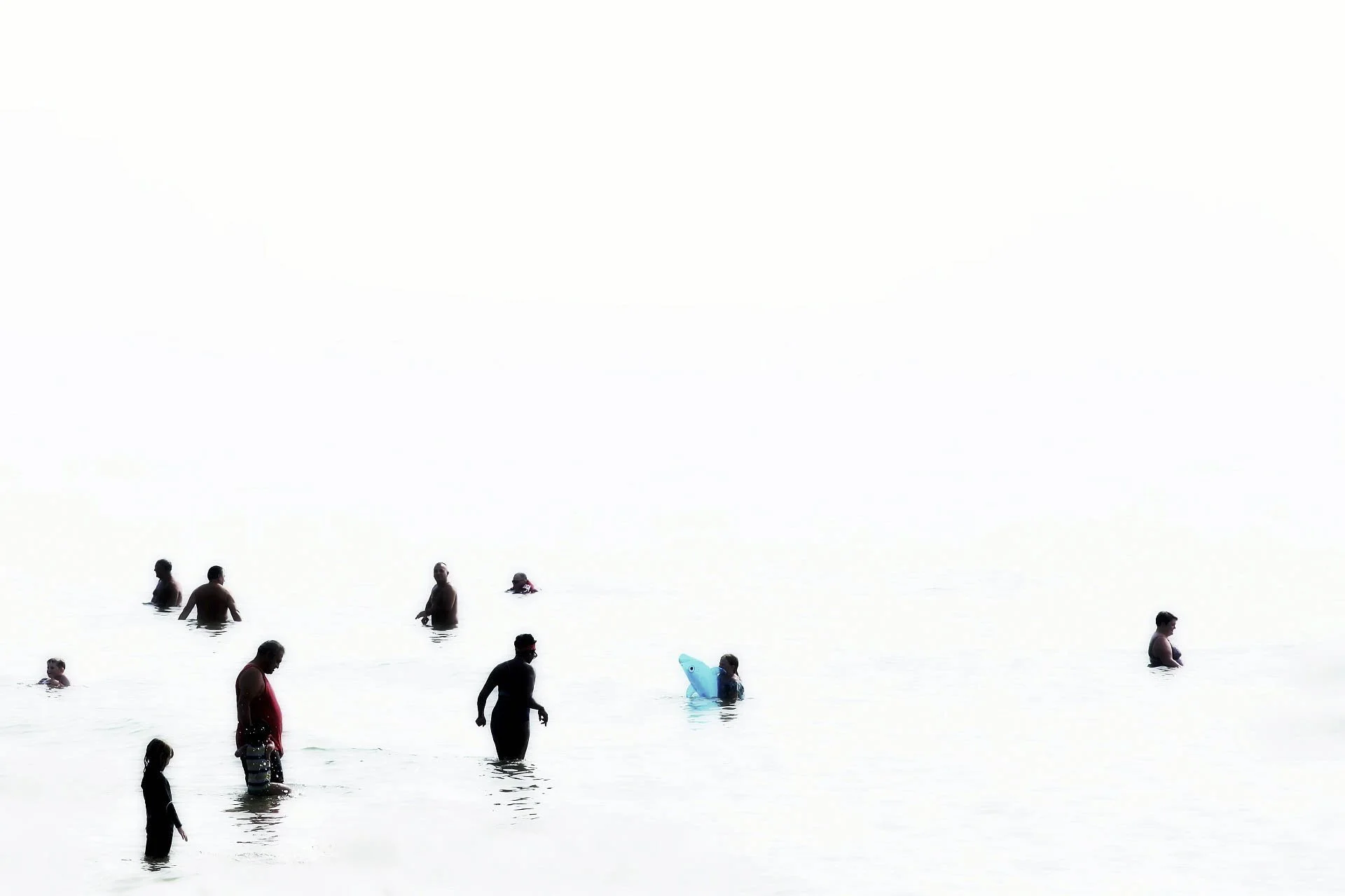 People swimming and wading in the ocean on a bright day.