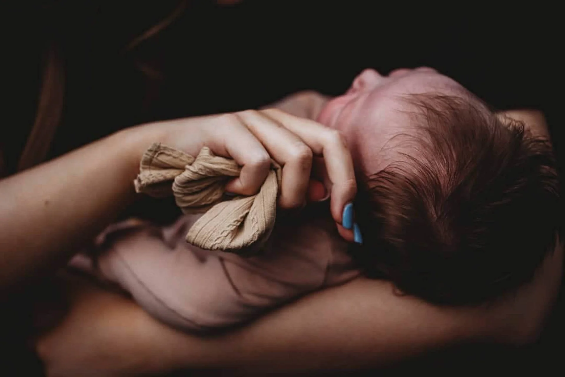 Close-up of a hand with painted nails holding a piece of fabric next to a baby's head.