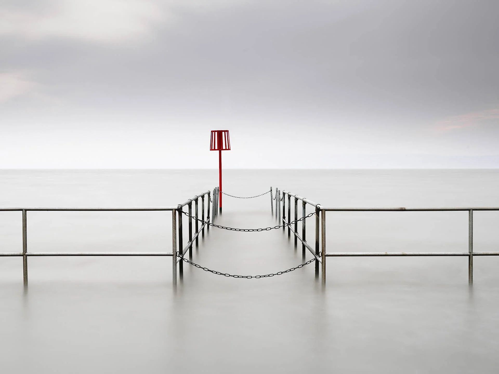 Calm seascape with metal railing walkway leading into the water and red navigation marker.