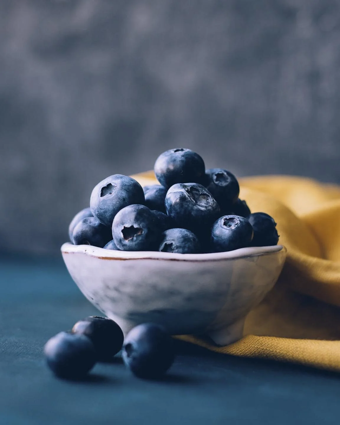 Bowl of fresh blueberries on a table with a yellow cloth in the background.