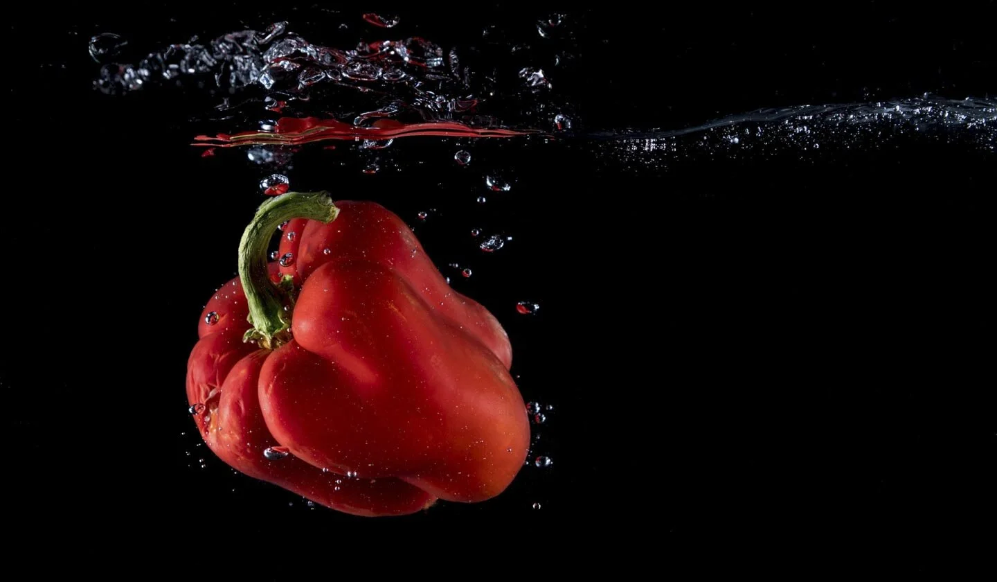 Red bell pepper submerged in water with bubbles against black background.