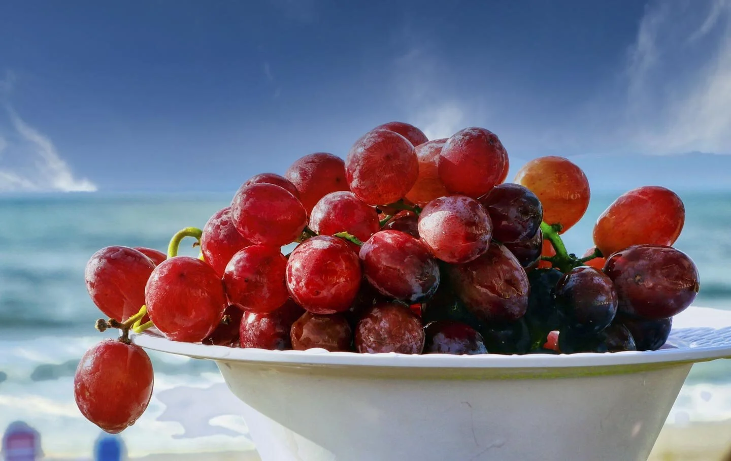 Bowl of red grapes on beach background