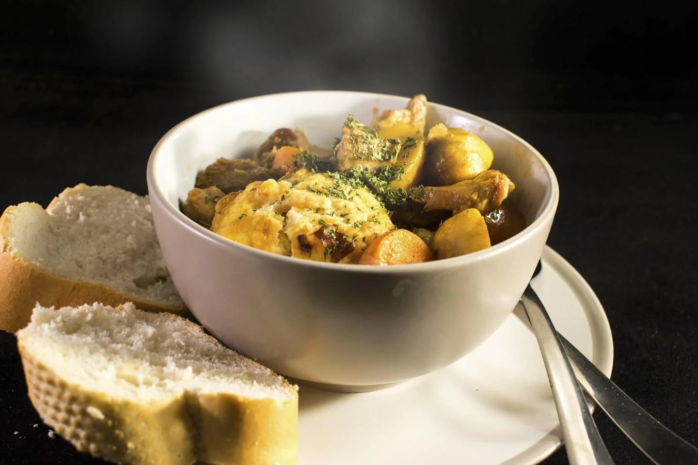 Bowl of beef stew with vegetables and dumpling, served with two slices of bread on a plate.