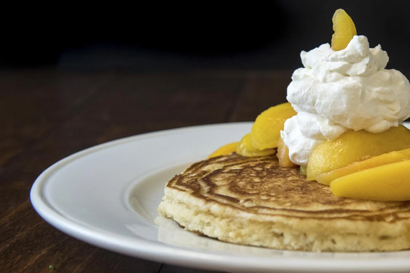 Pancake with peaches and whipped cream on a plate.