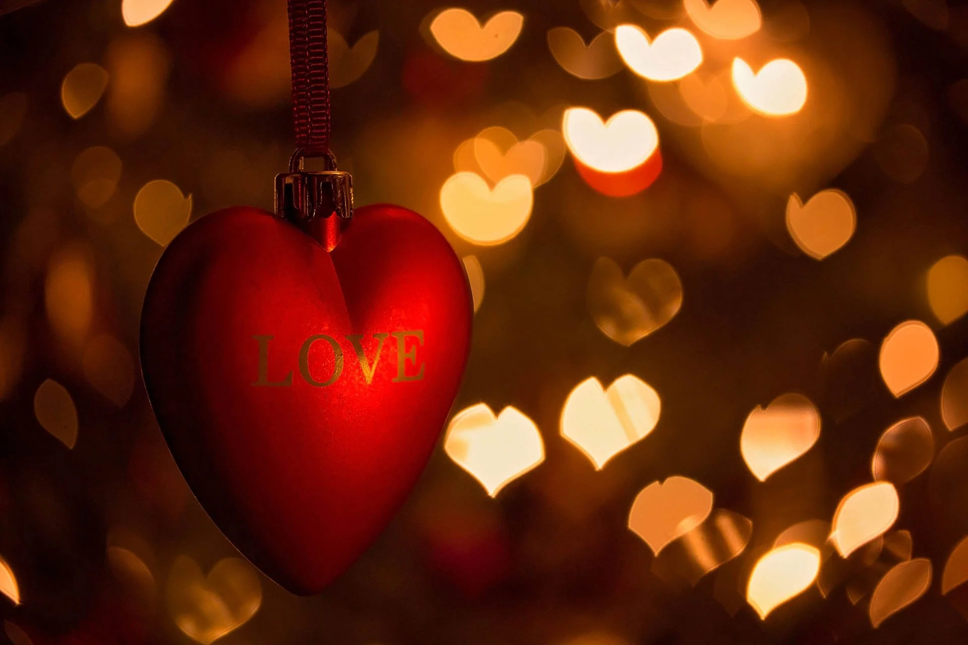 Red heart ornament with 'LOVE' text, surrounded by golden heart-shaped bokeh lights.