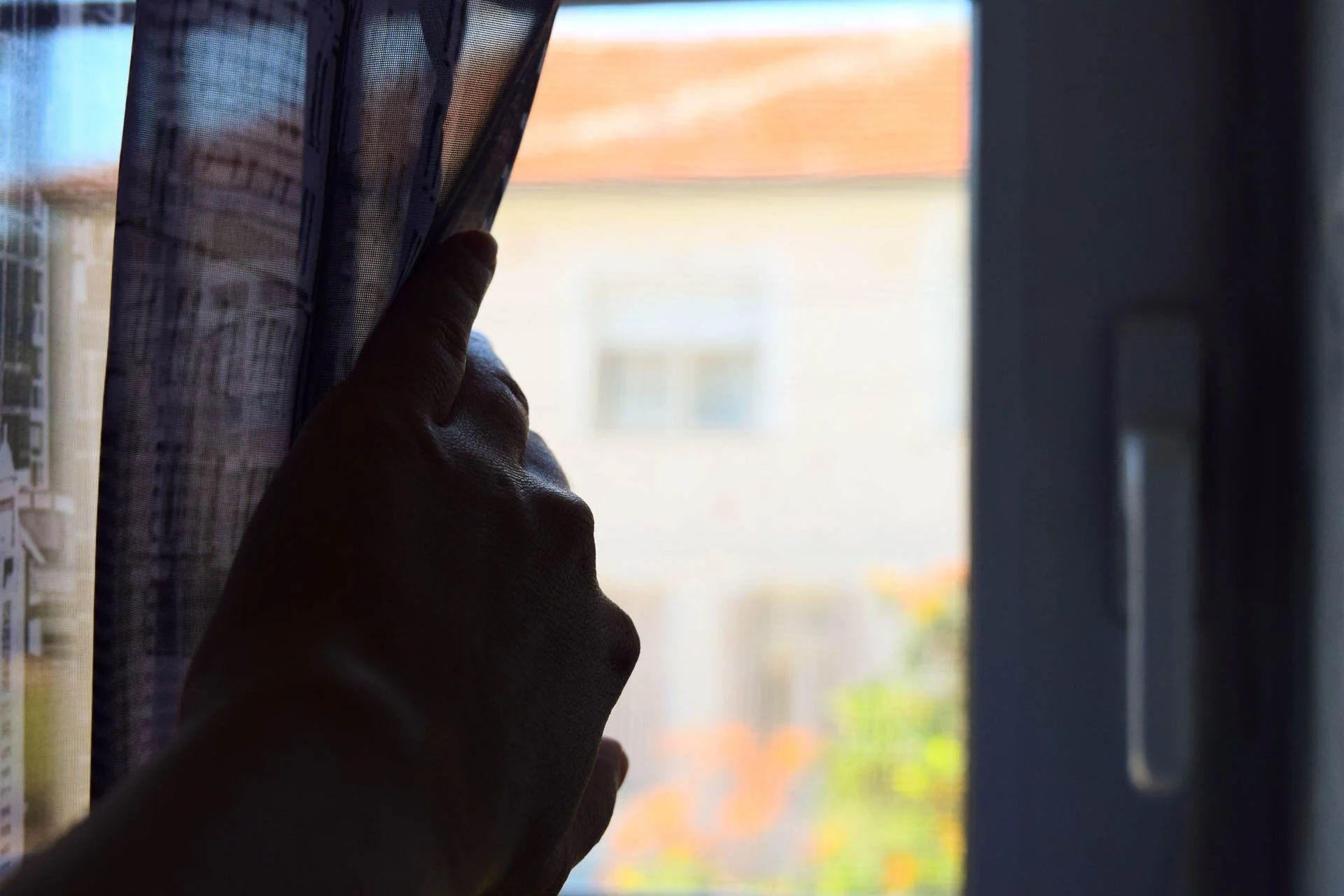 Hand pulling back a curtain to look out a window