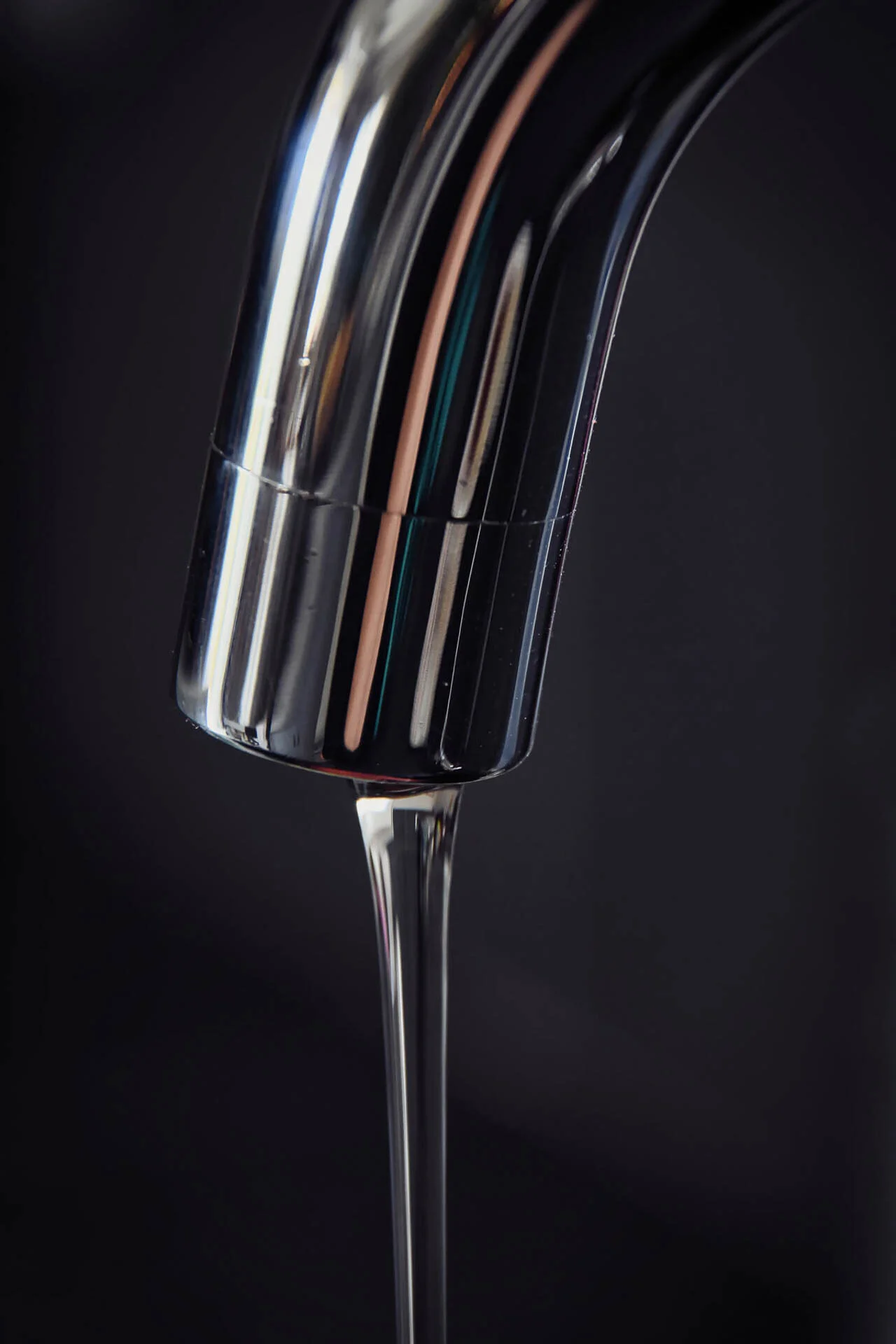 Close-up of a shiny metal faucet with water flowing against a dark background.