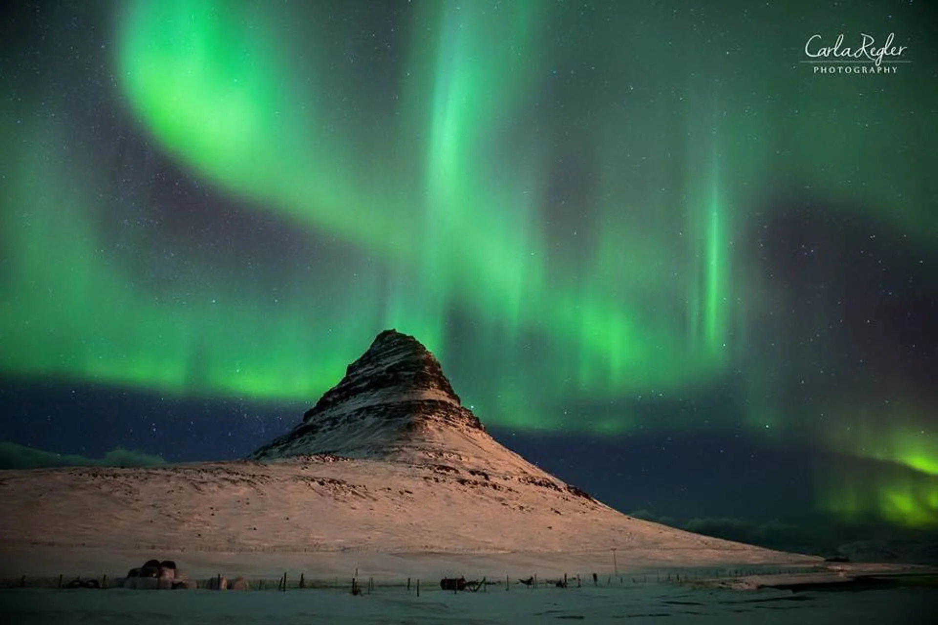 Northern lights over snow-covered mountain at night in Iceland.