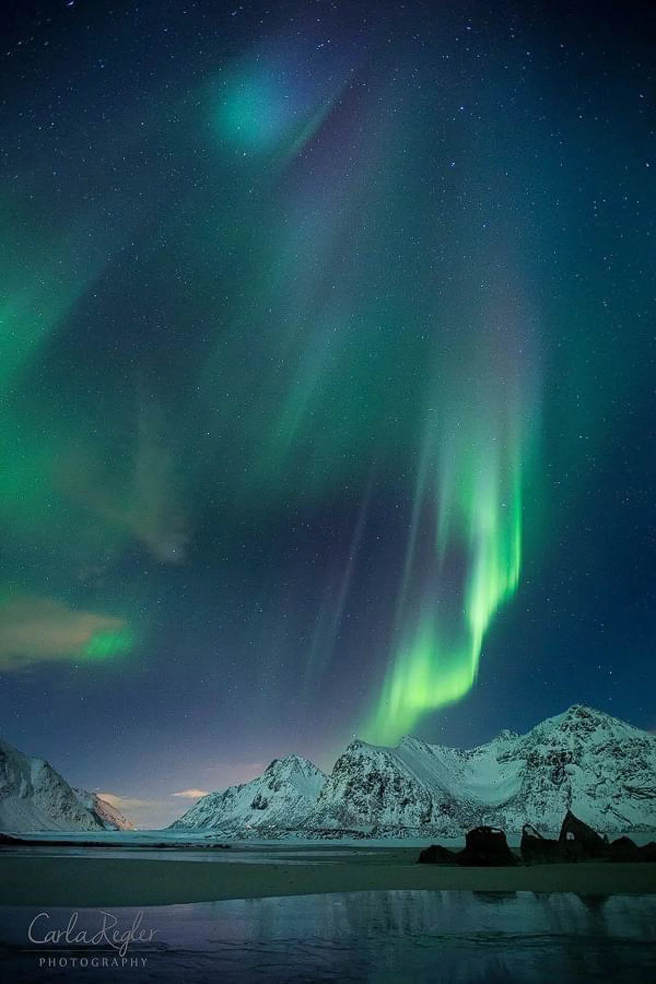 Aurora borealis over snow-covered mountains at night, with a clear starry sky and green, purple, and blue lights.