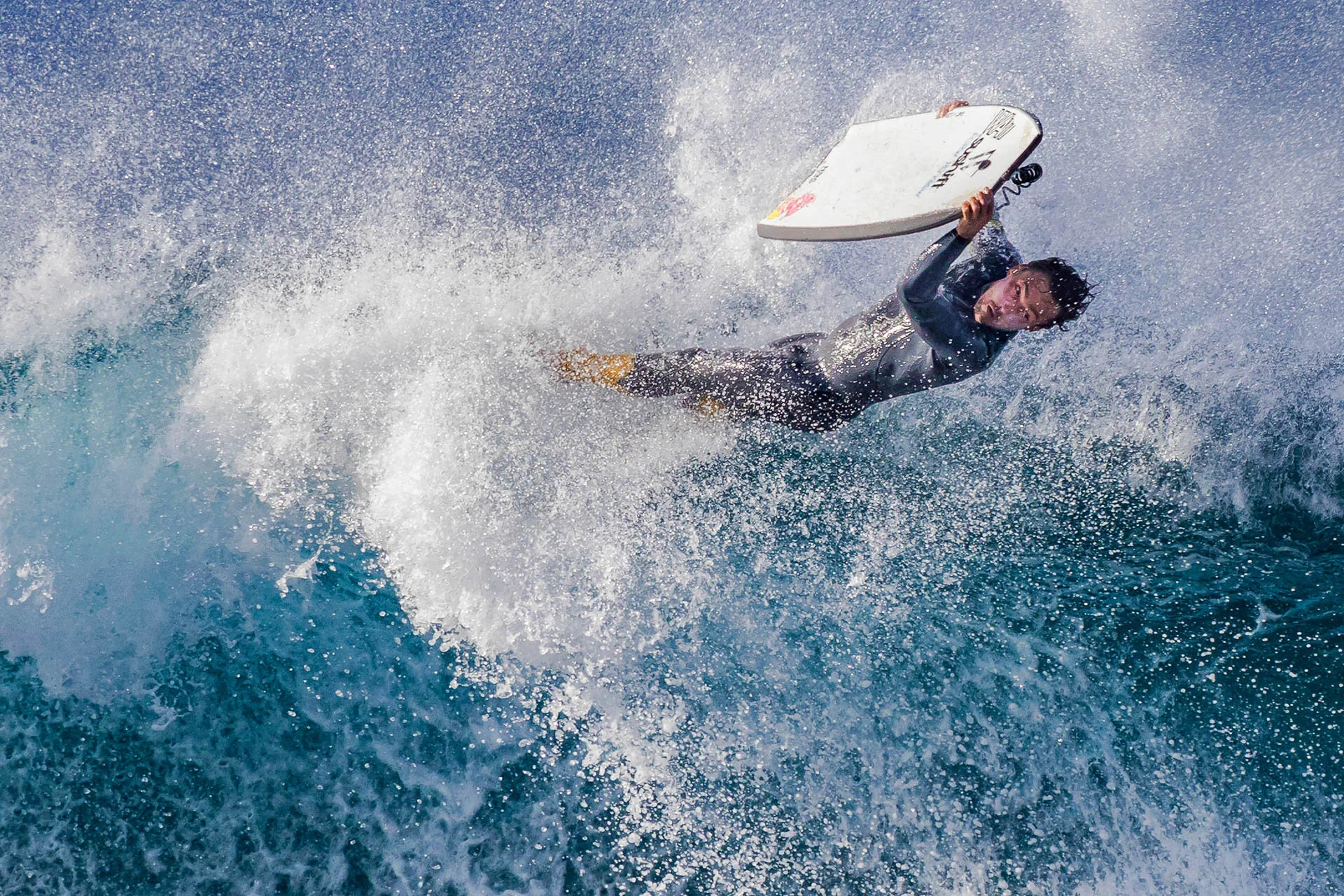 A person wearing a wetsuit is surfing and performing a maneuver on a wave, with water splashing around.