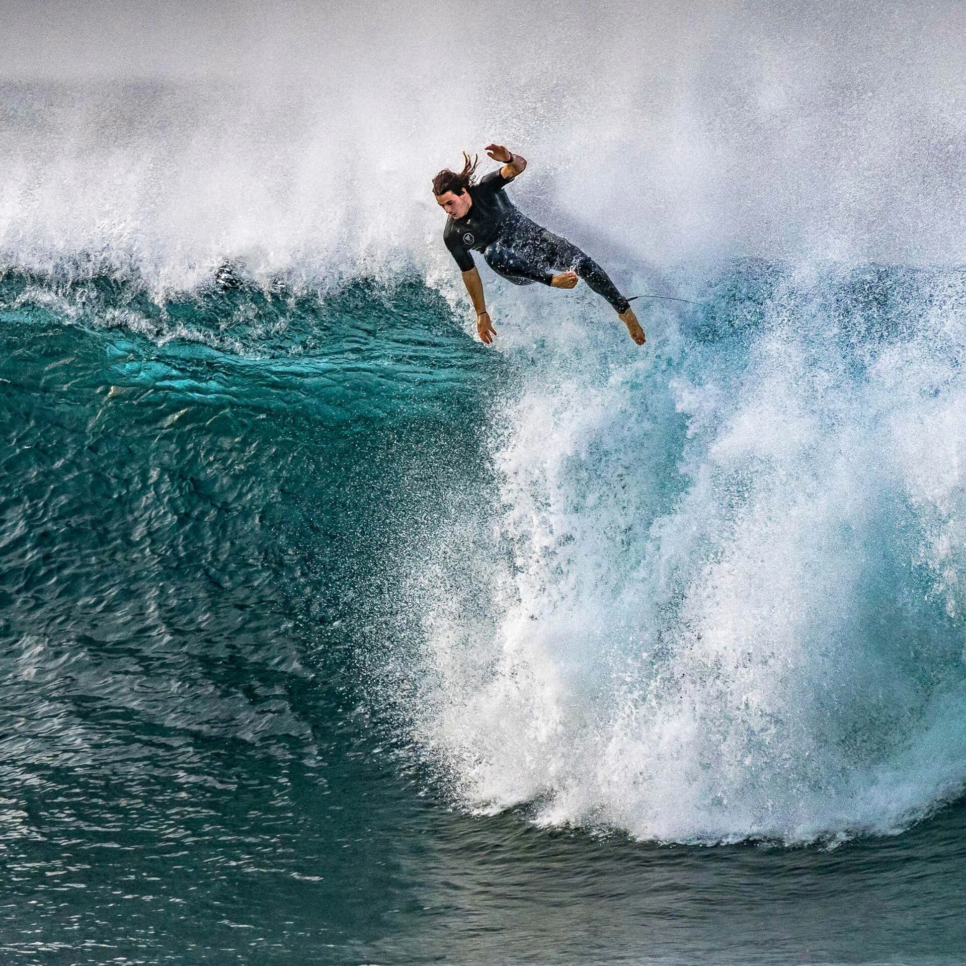 Surfer in black wetsuit falling off a large wave in the ocean.
