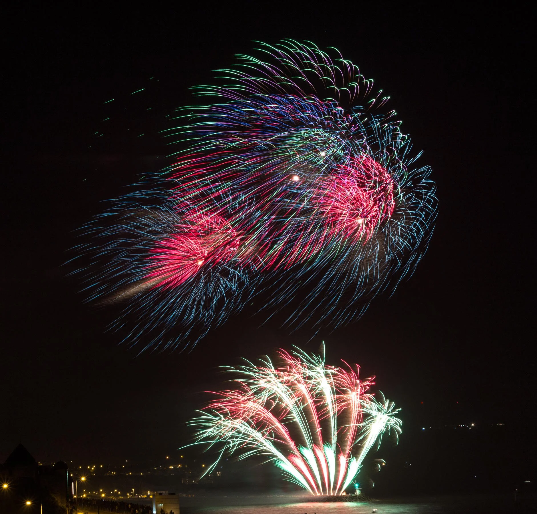 Colorful fireworks display with red, green, and blue streaks against night sky.