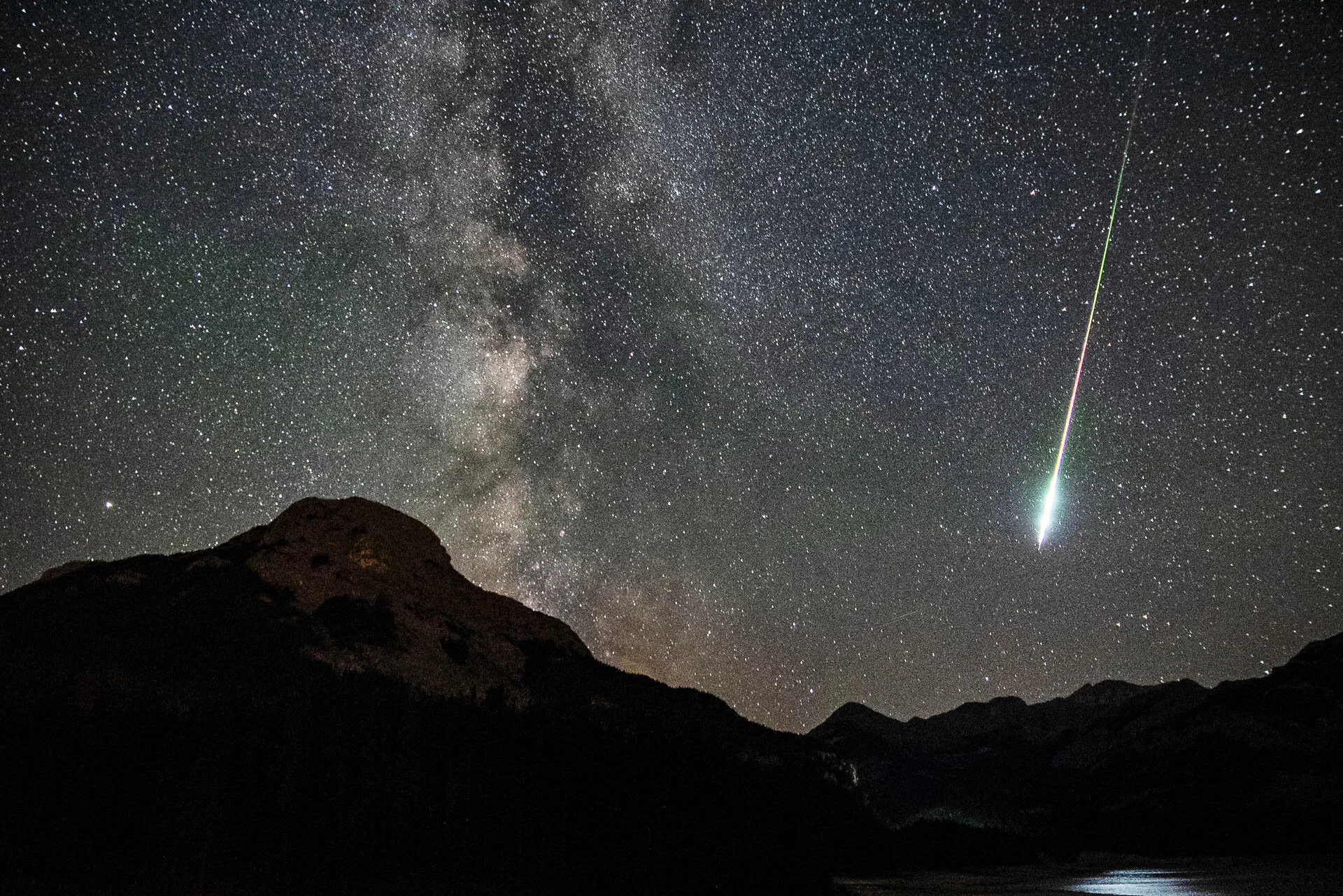Night sky with Milky Way and meteor over mountain silhouette