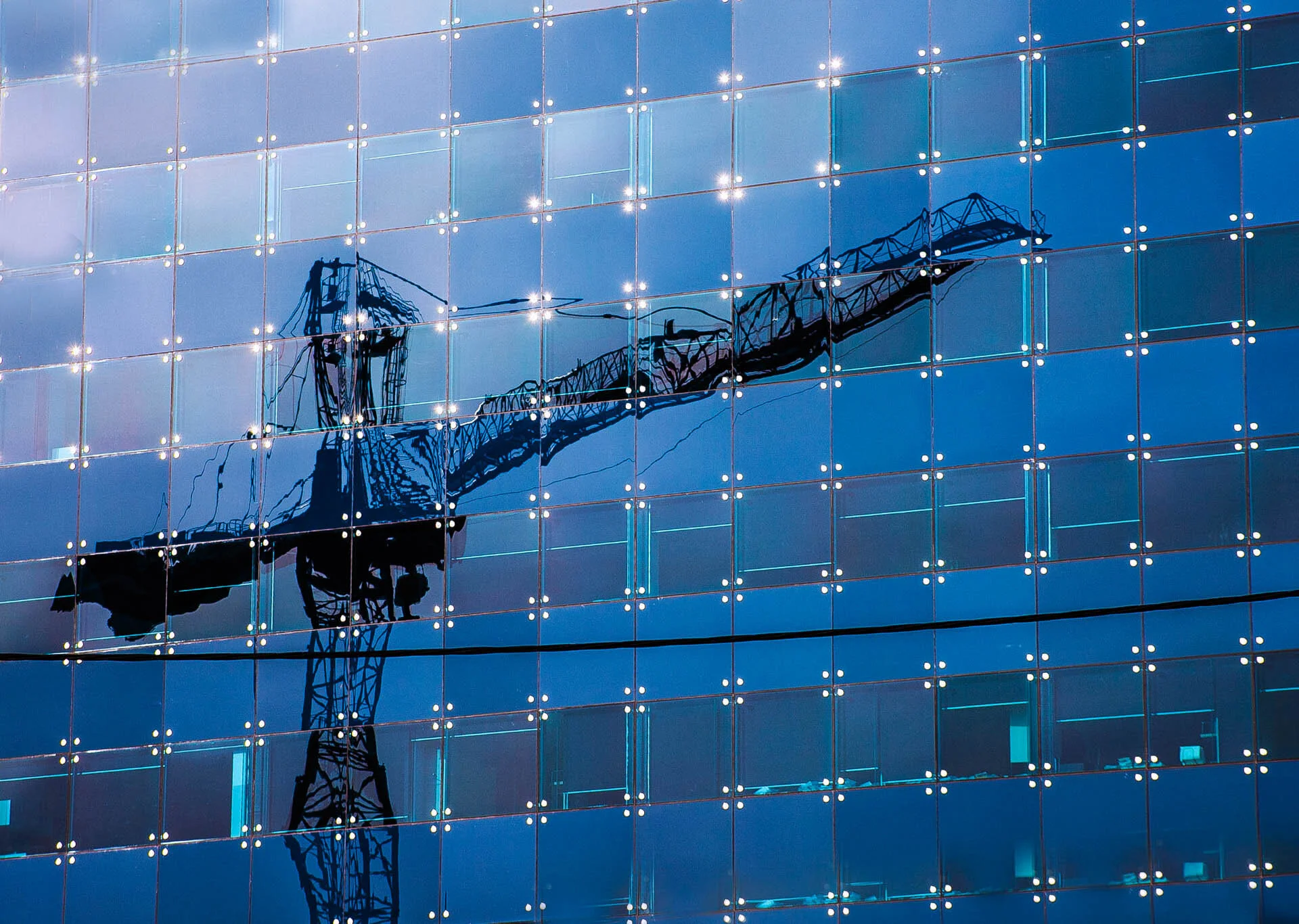 Reflection of a construction crane on a glass building facade.