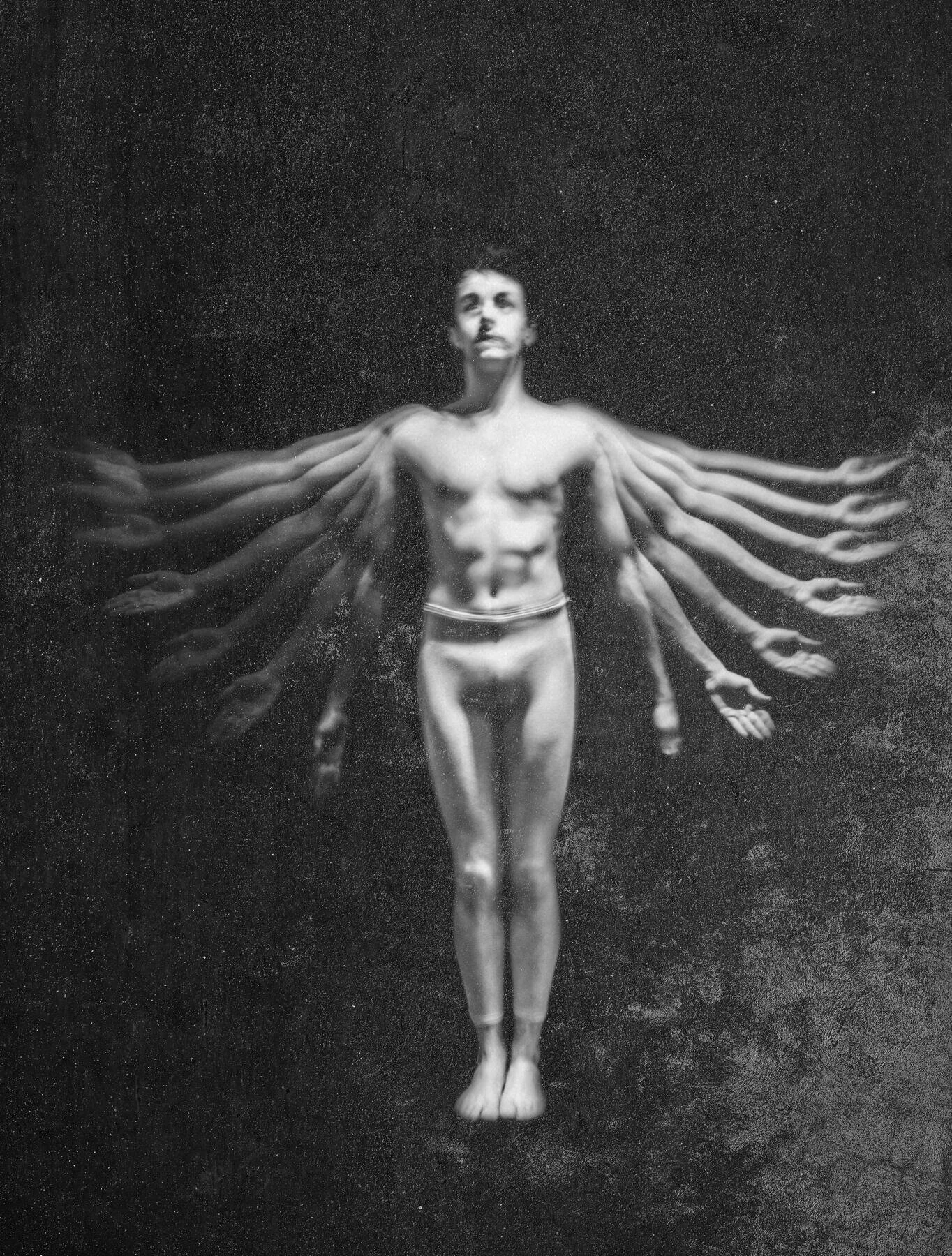 Surreal image of a shirtless person with multiple blurred arms outstretched against a dark background.
