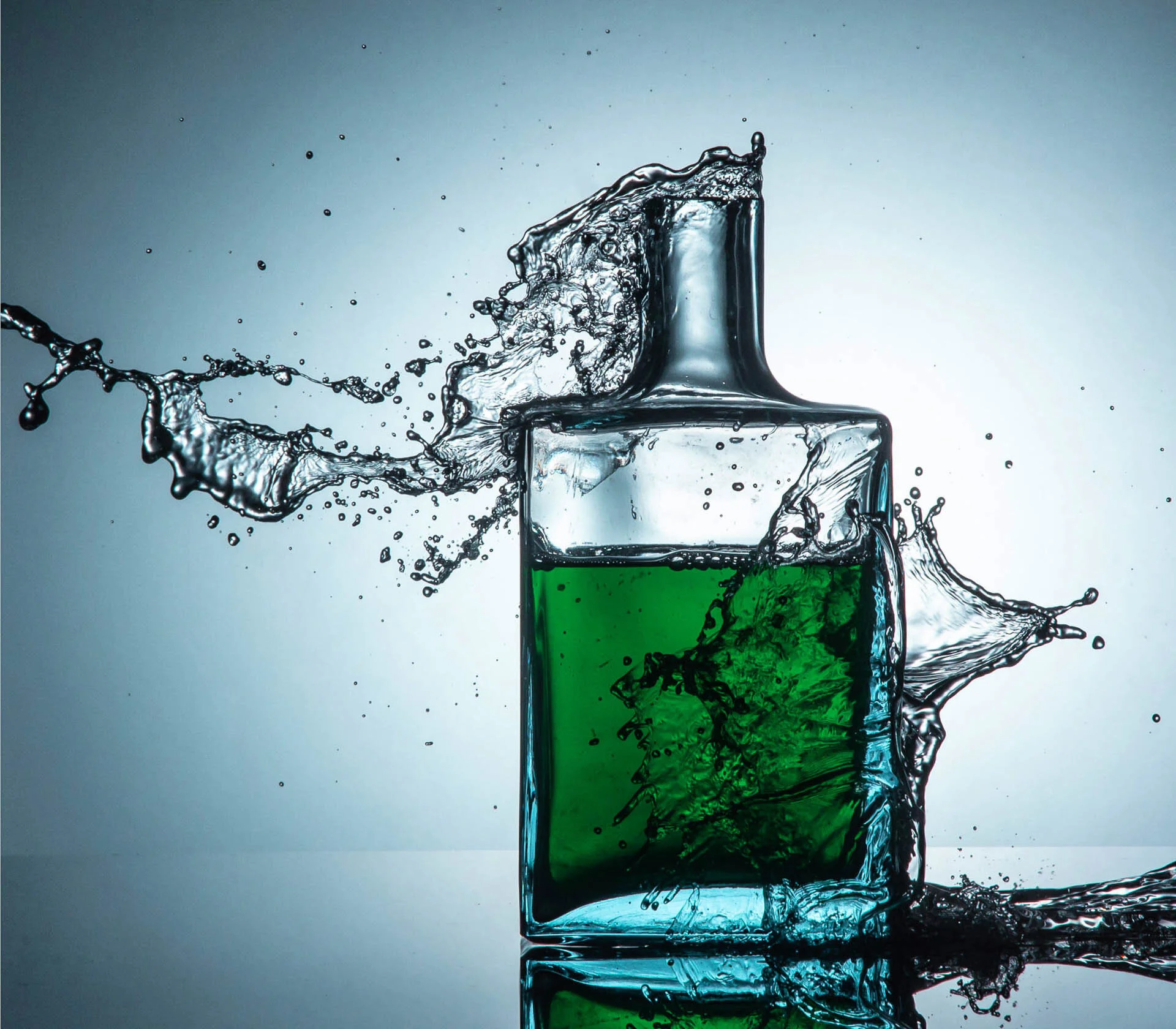 Glass bottle with green liquid splashing out