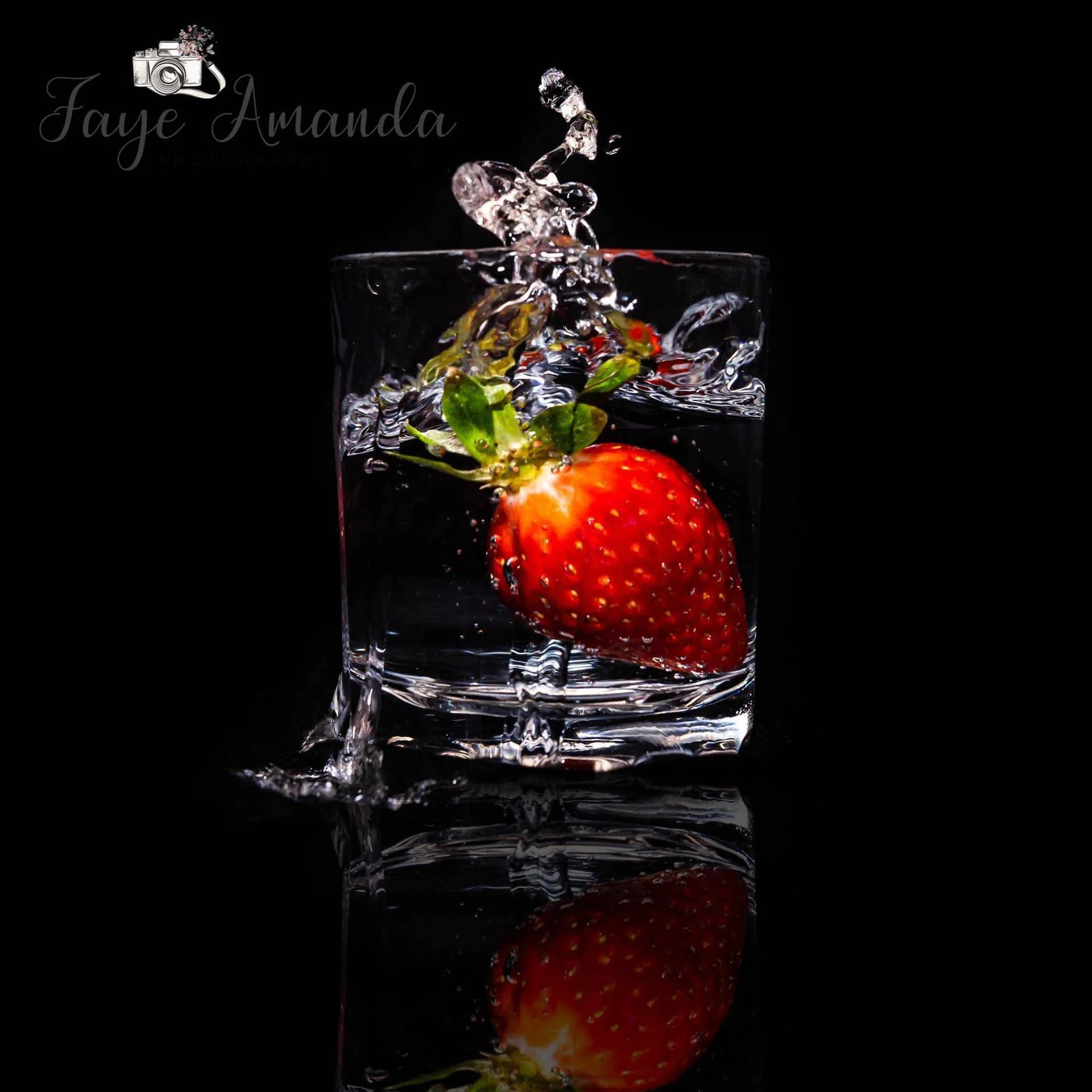 A strawberry splashing into a glass of water against a black background.