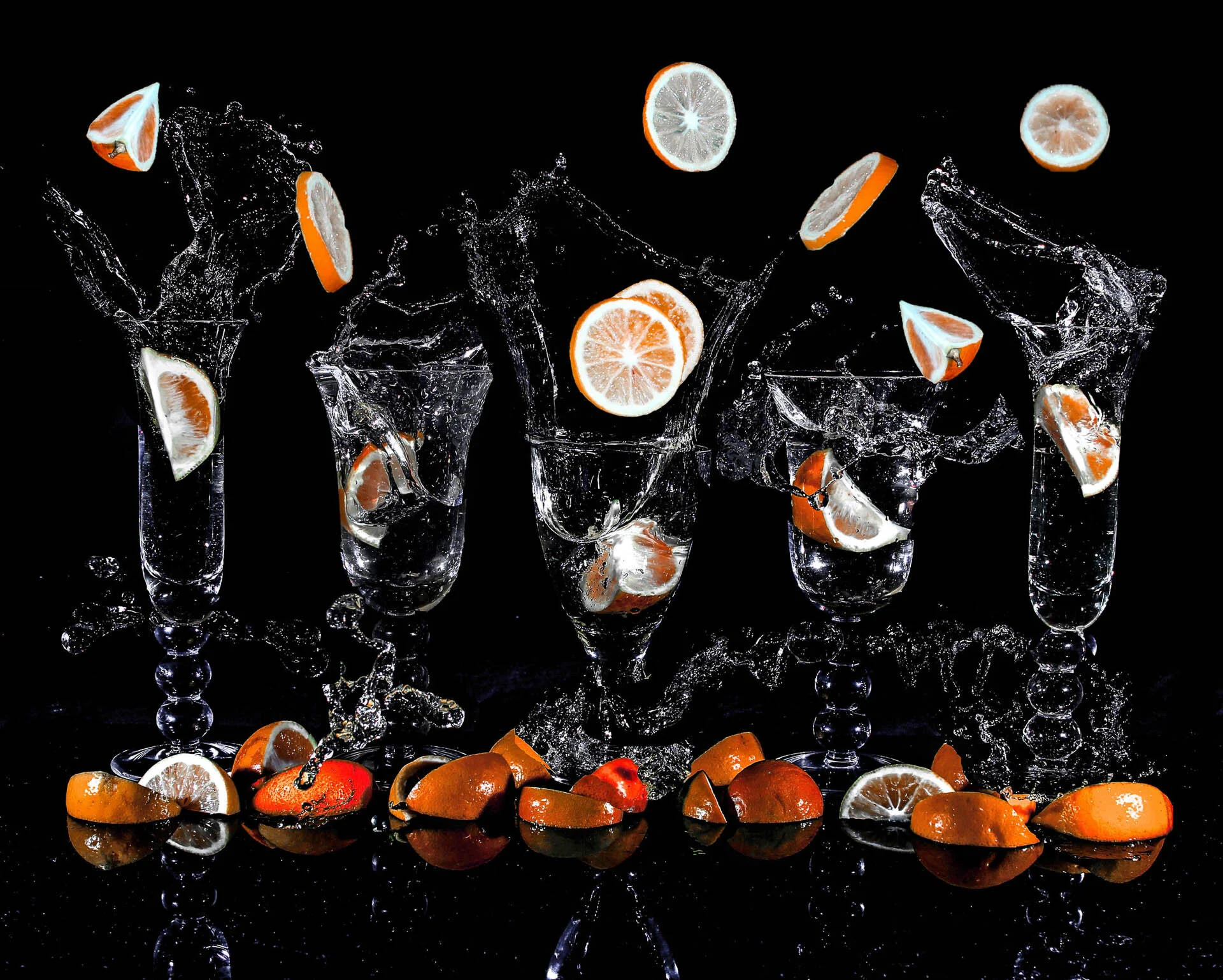 Slices of citrus fruit splashing into clear glasses of water against a black background, with water droplets and fruit pieces scattered.