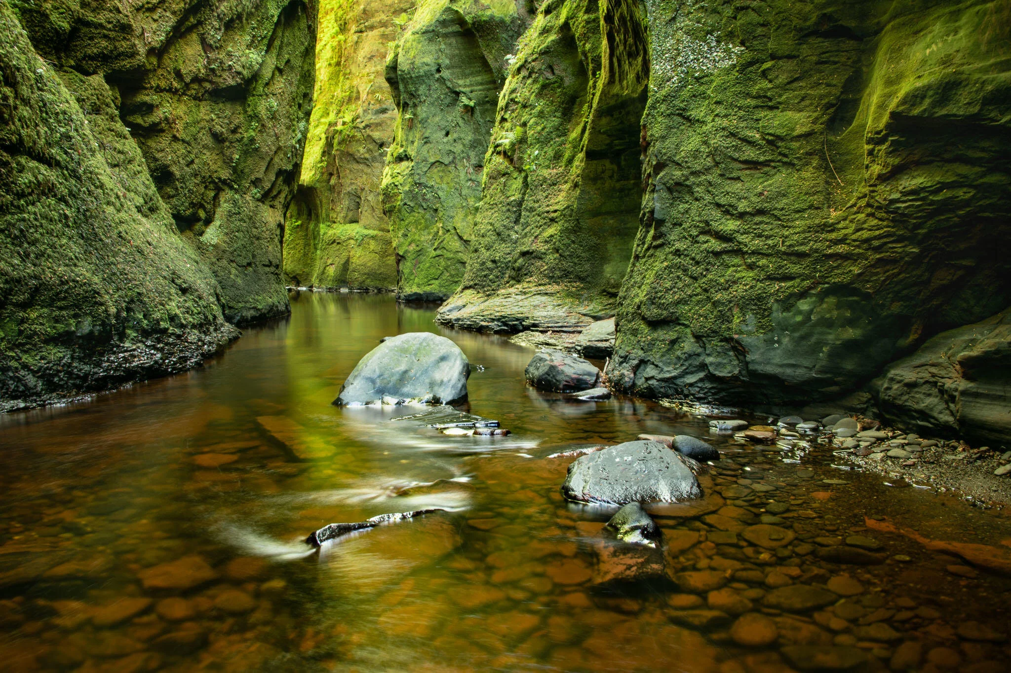 Narrow gorge with moss-covered walls and shallow stream.