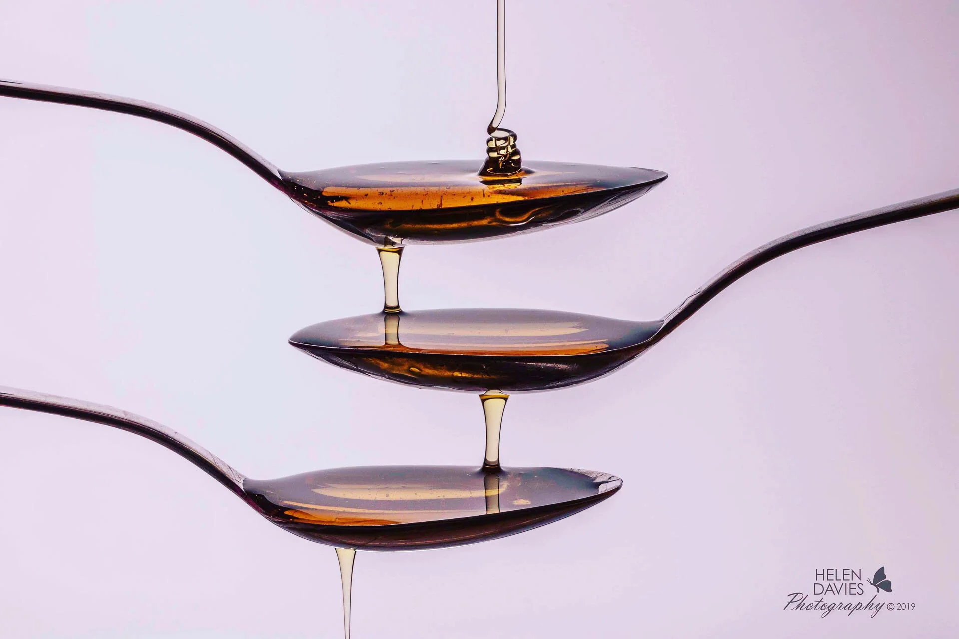 Three spoons stacked with honey dripping between them against a white background.