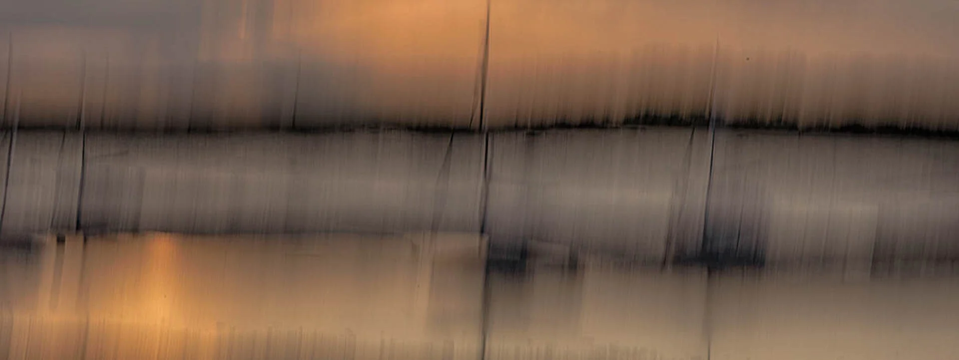 Abstract blurred image with vertical streaks in warm and cool tones, resembling water reflections at sunset.