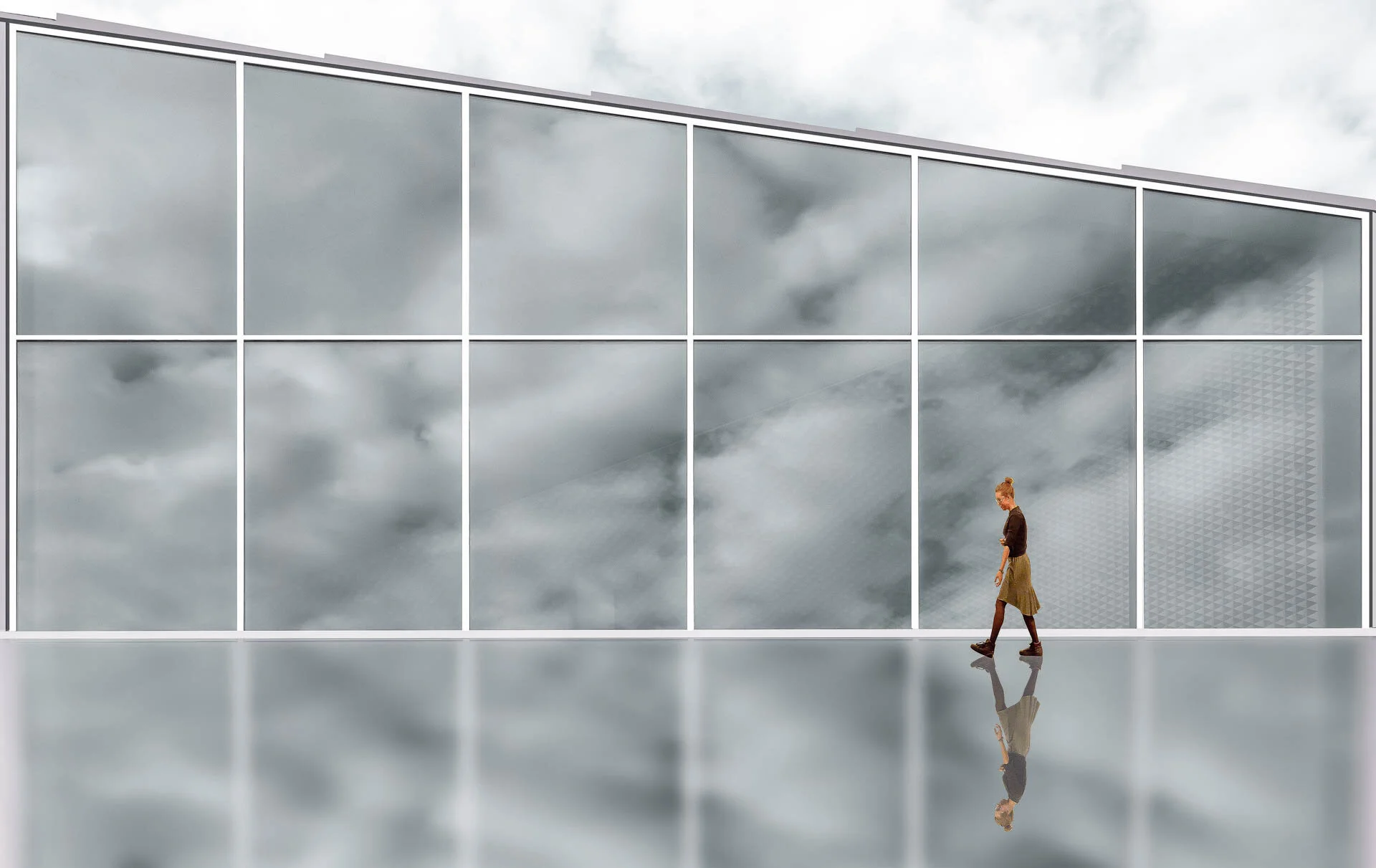 Person walking along a modern glass facade with cloudy reflections.