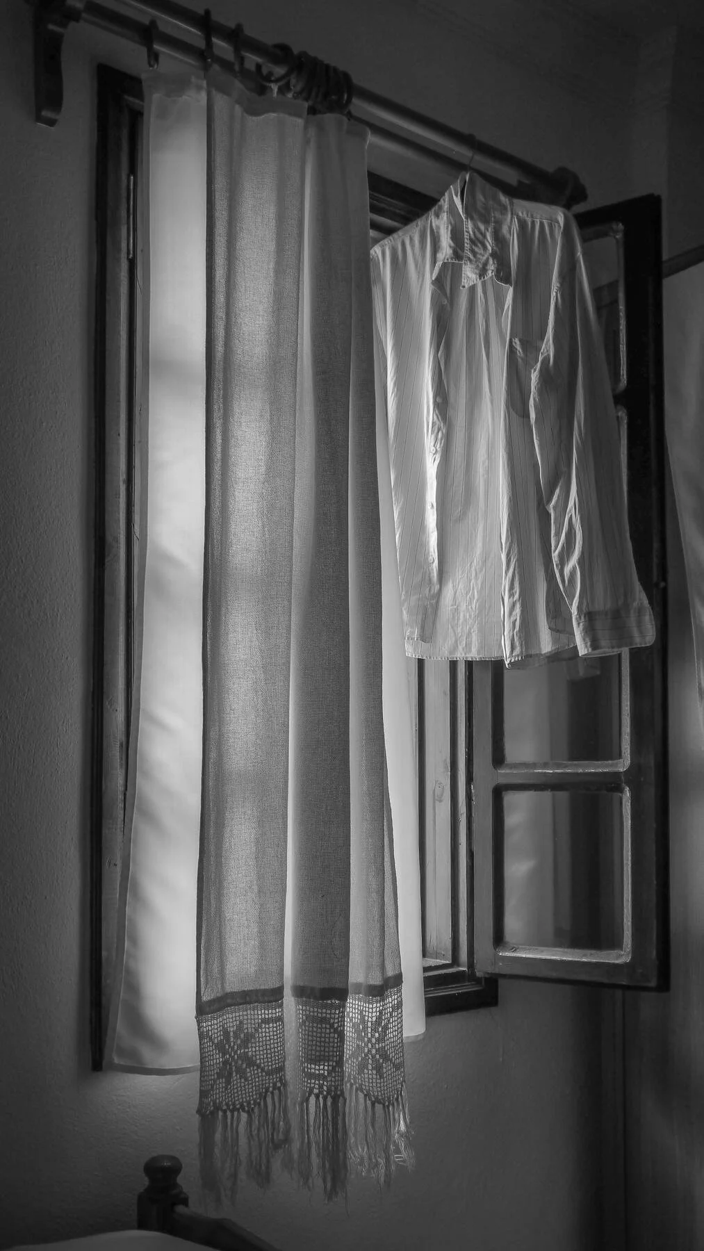Black and white photo of an open window with sheer curtains and a white shirt hanging on a hanger.
