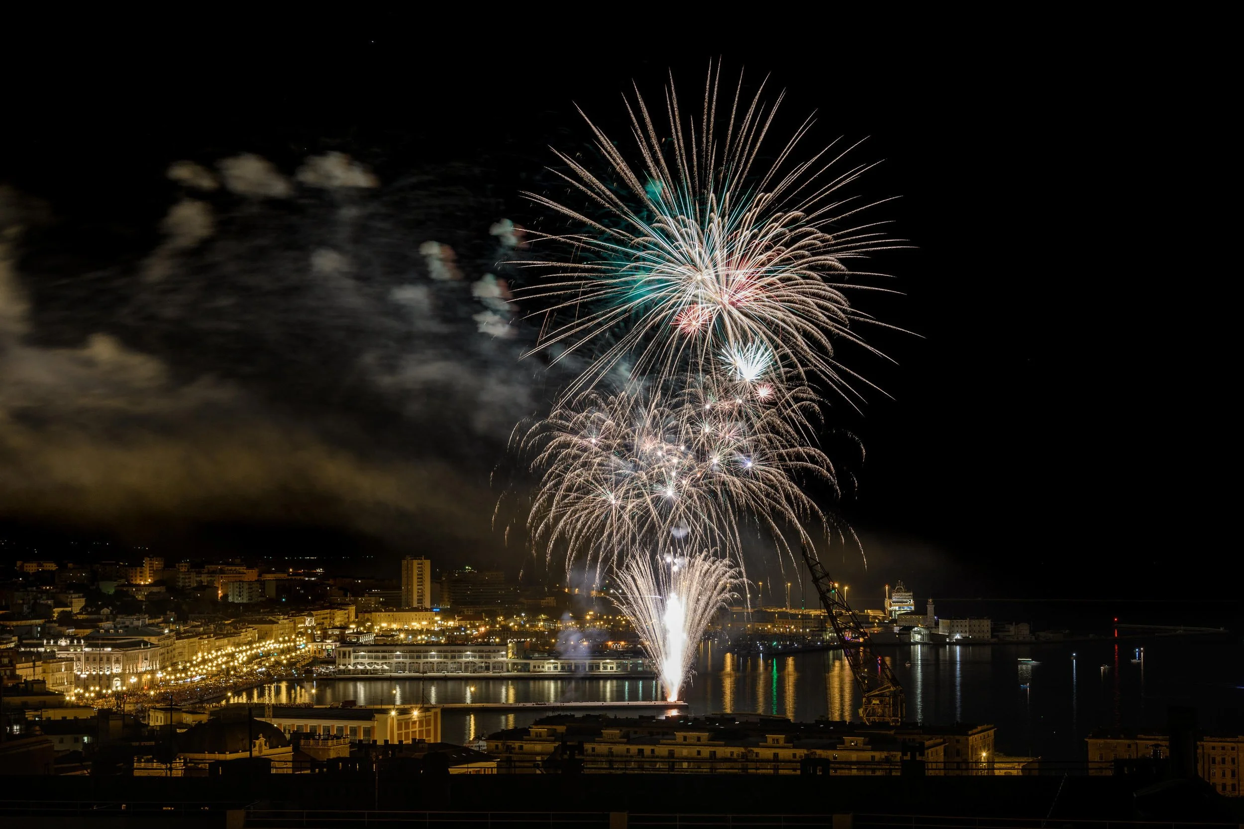 Fireworks display over a city waterfront at night.