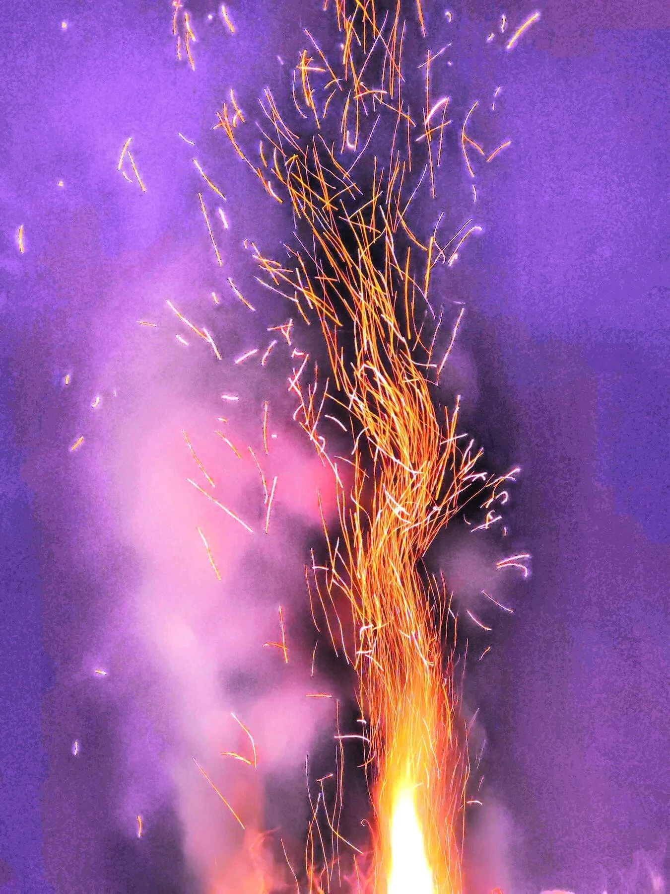 Bright sparks and colorful smoke from a fire against a purple night sky.