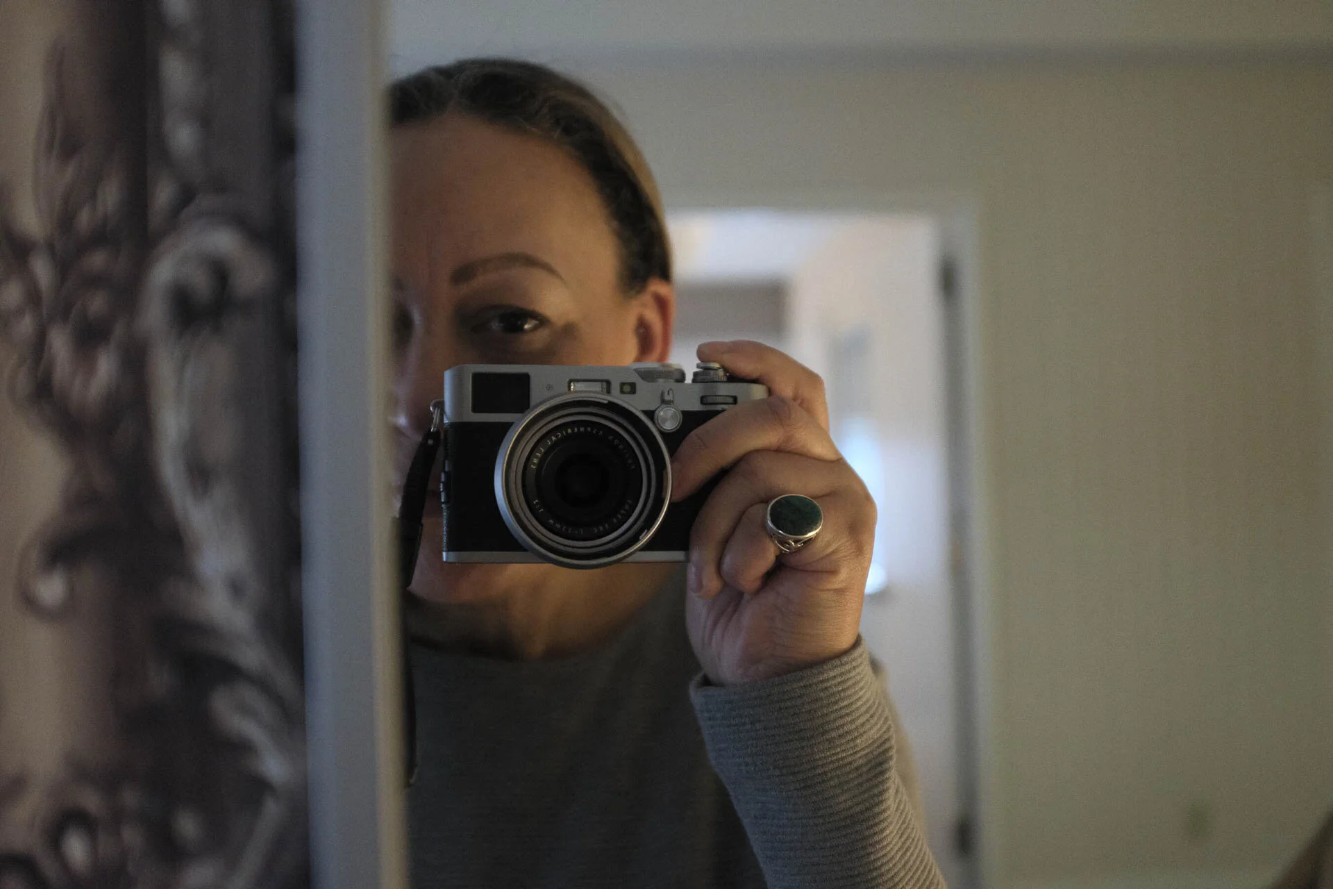 Person taking a mirror selfie with a camera, partially visible face, wearing a ring on their hand.