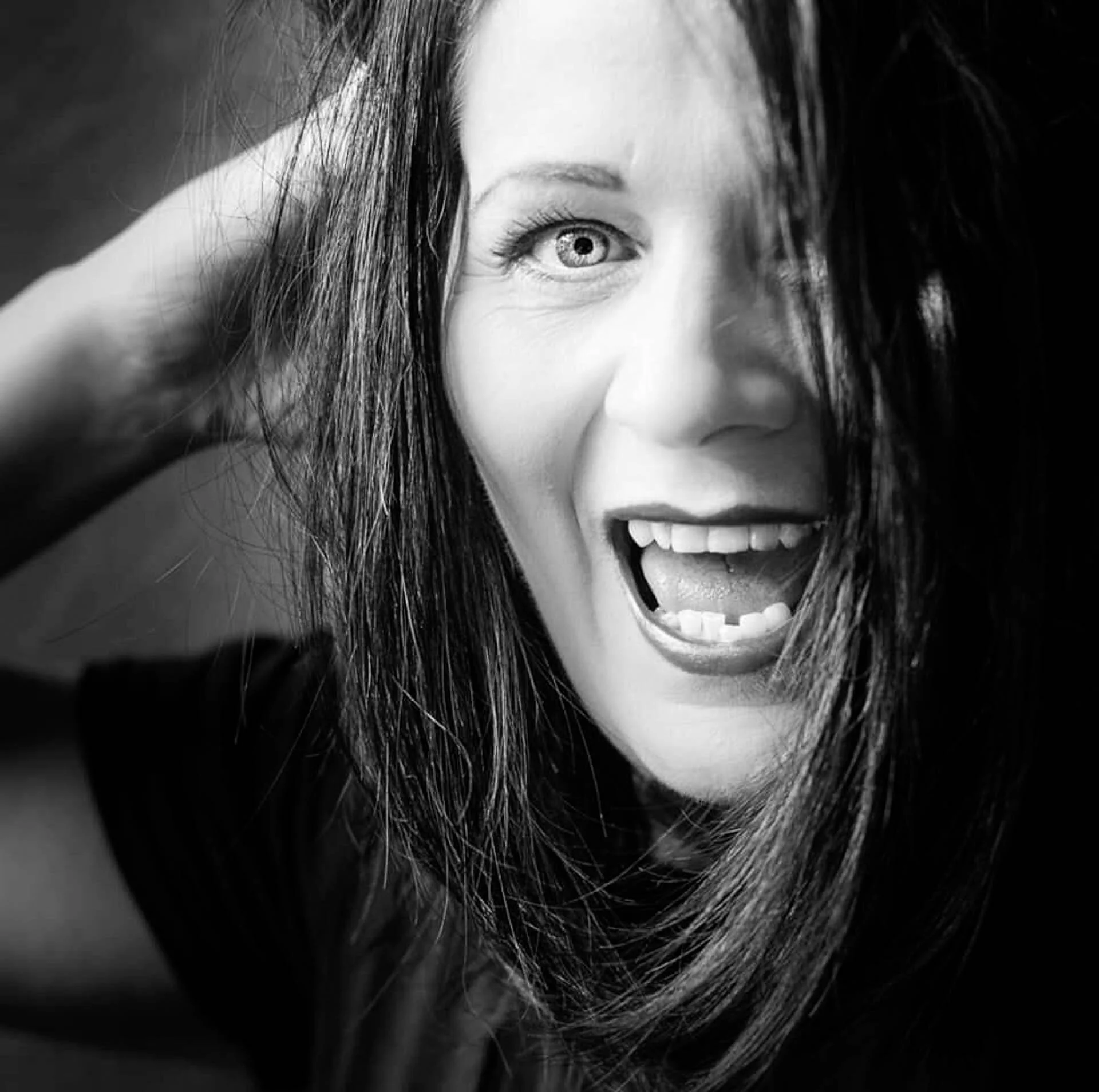 A black and white portrait of a smiling woman with long hair covering one eye.