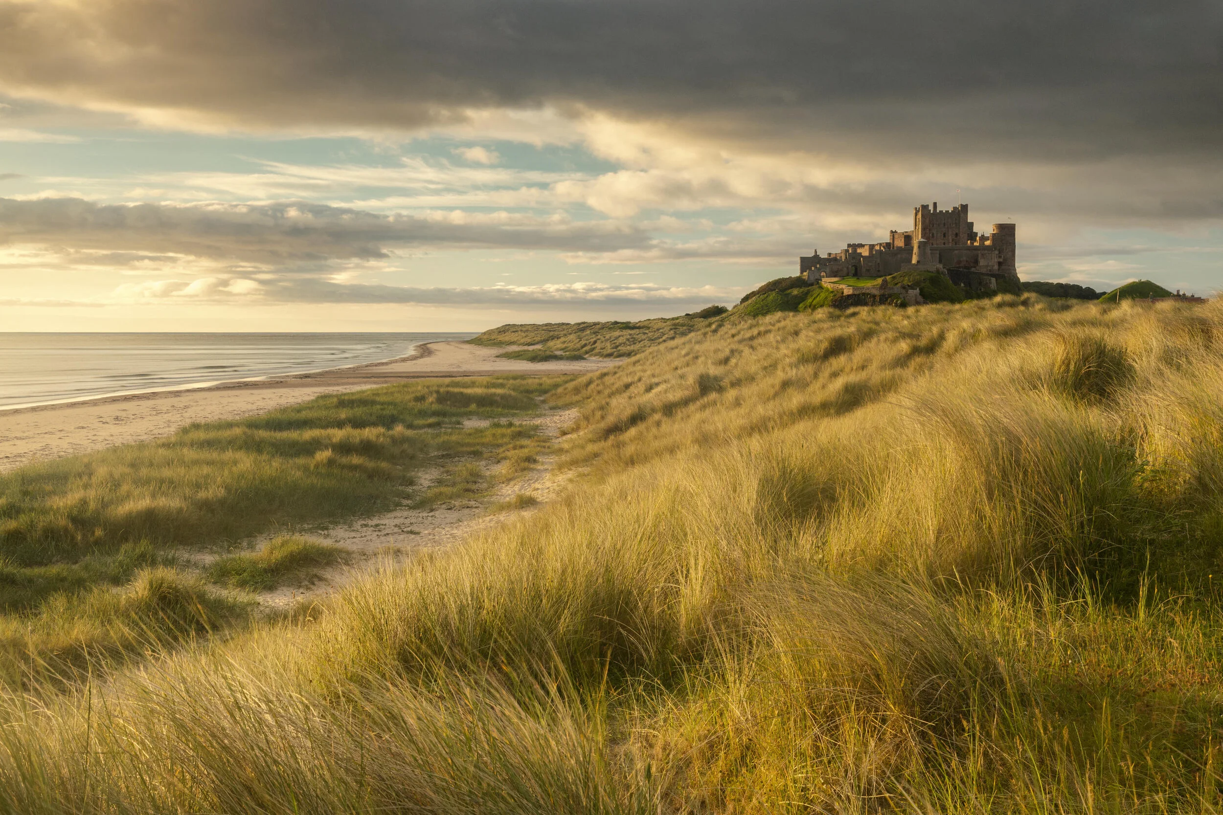 Coastal landscape with sand dunes and castle under cloudy sky