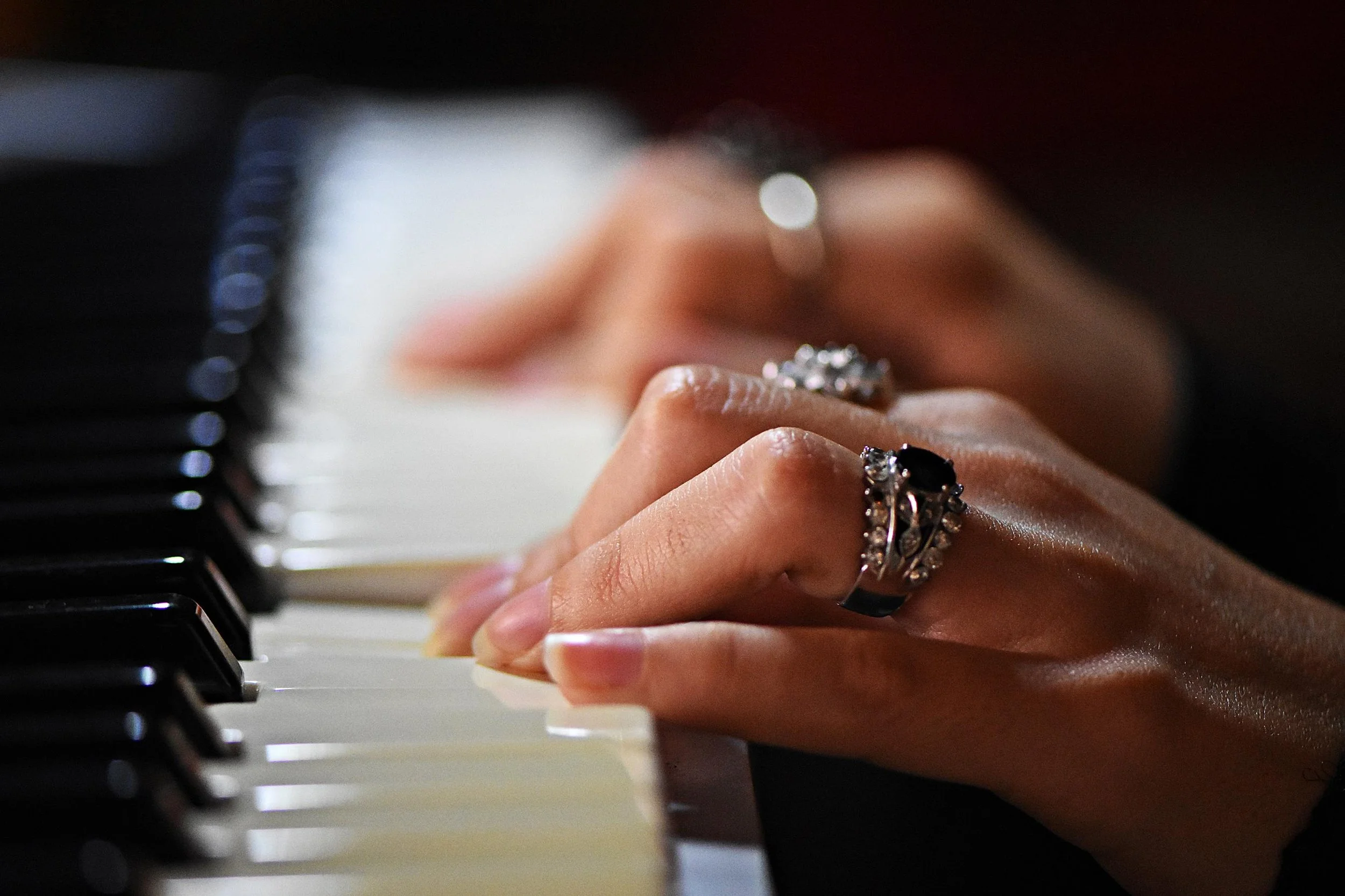 Close-up of hands playing piano keys with jewelry on fingers.