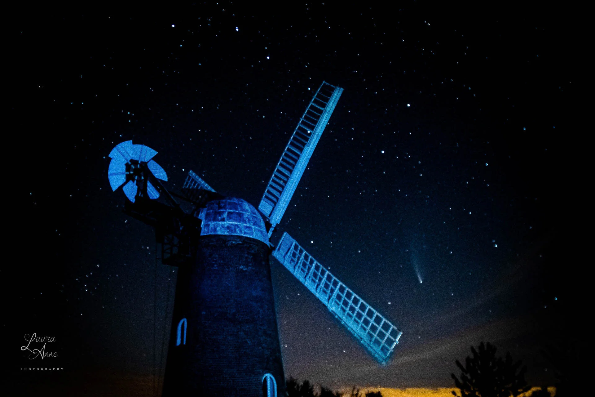 Silhouette of a windmill against a starry night sky with a visible comet.