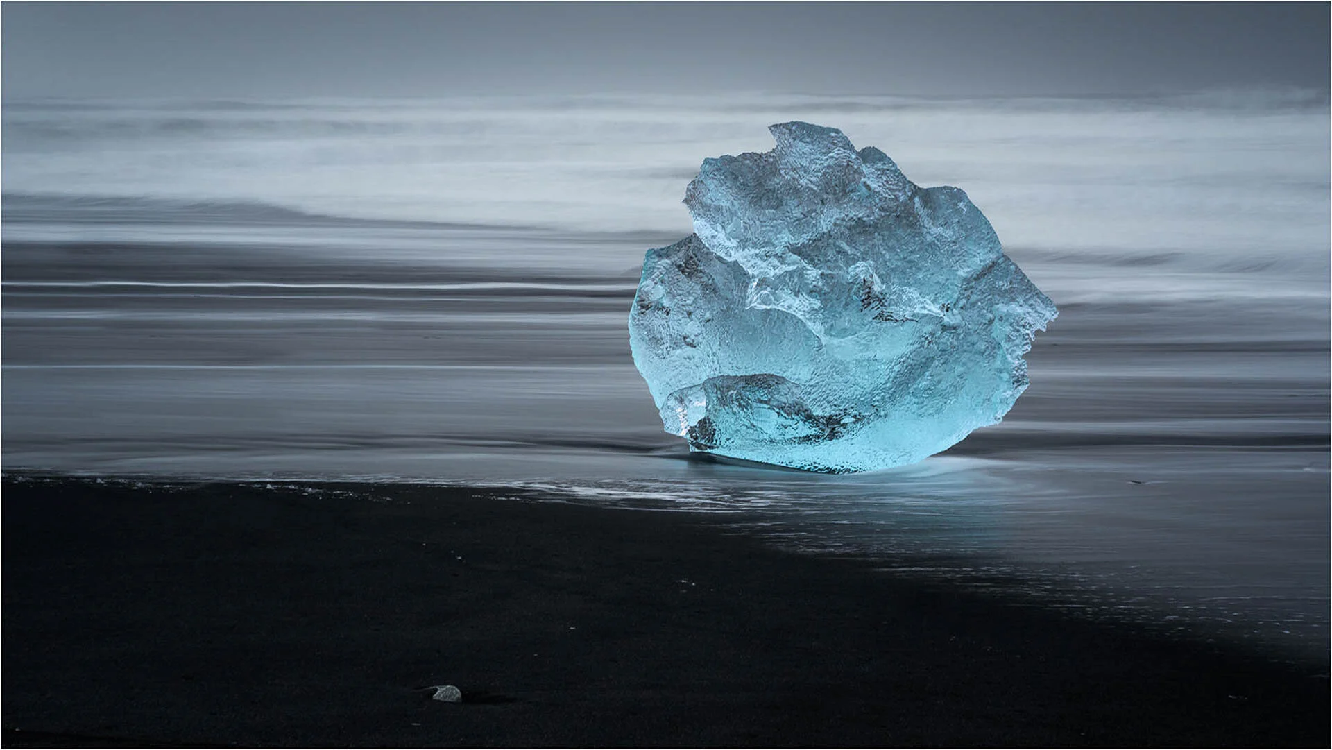 Large blue ice block on beach with blurred ocean in background