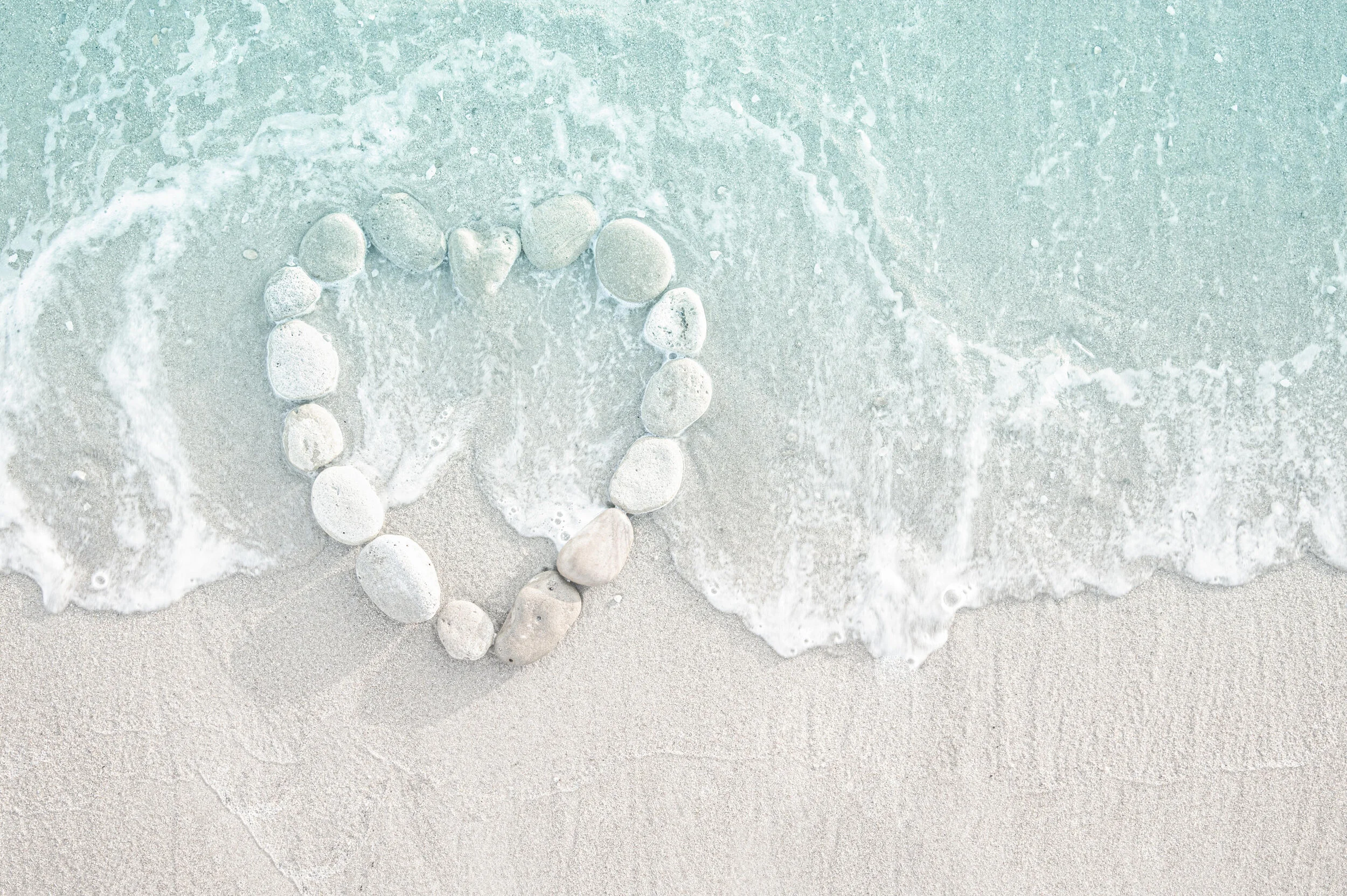 Heart shape made of stones on sandy beach with waves.