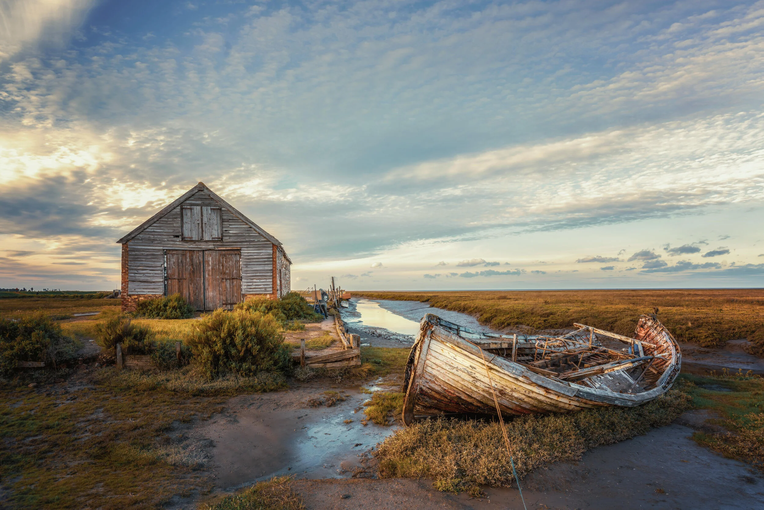 Old wooden barn and abandoned boat on marshland at sunset