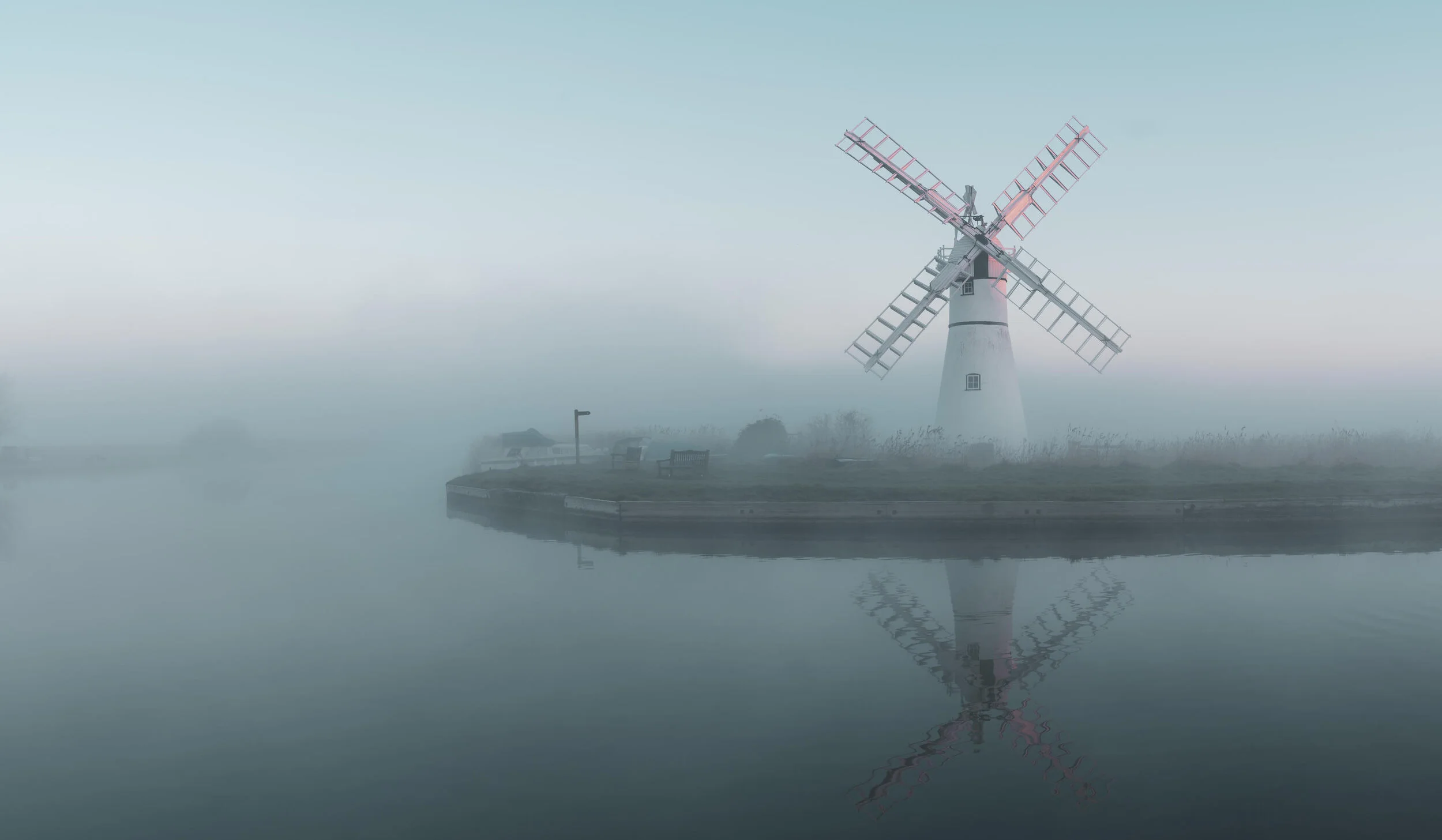 Windmill on a foggy landscape with a reflection in the water.