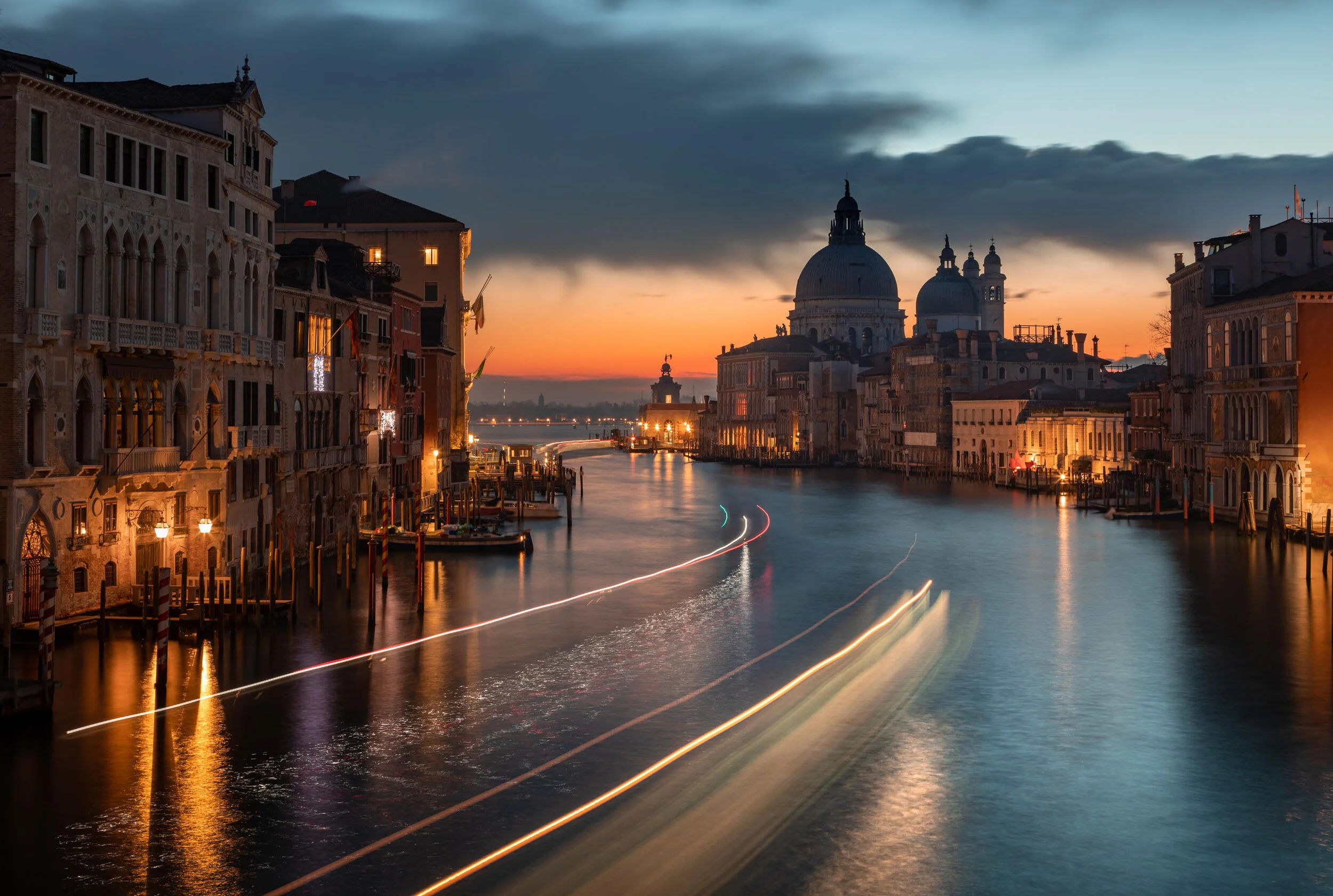 Grand Canal in Venice at sunset with illuminated buildings and blurred boat lights.