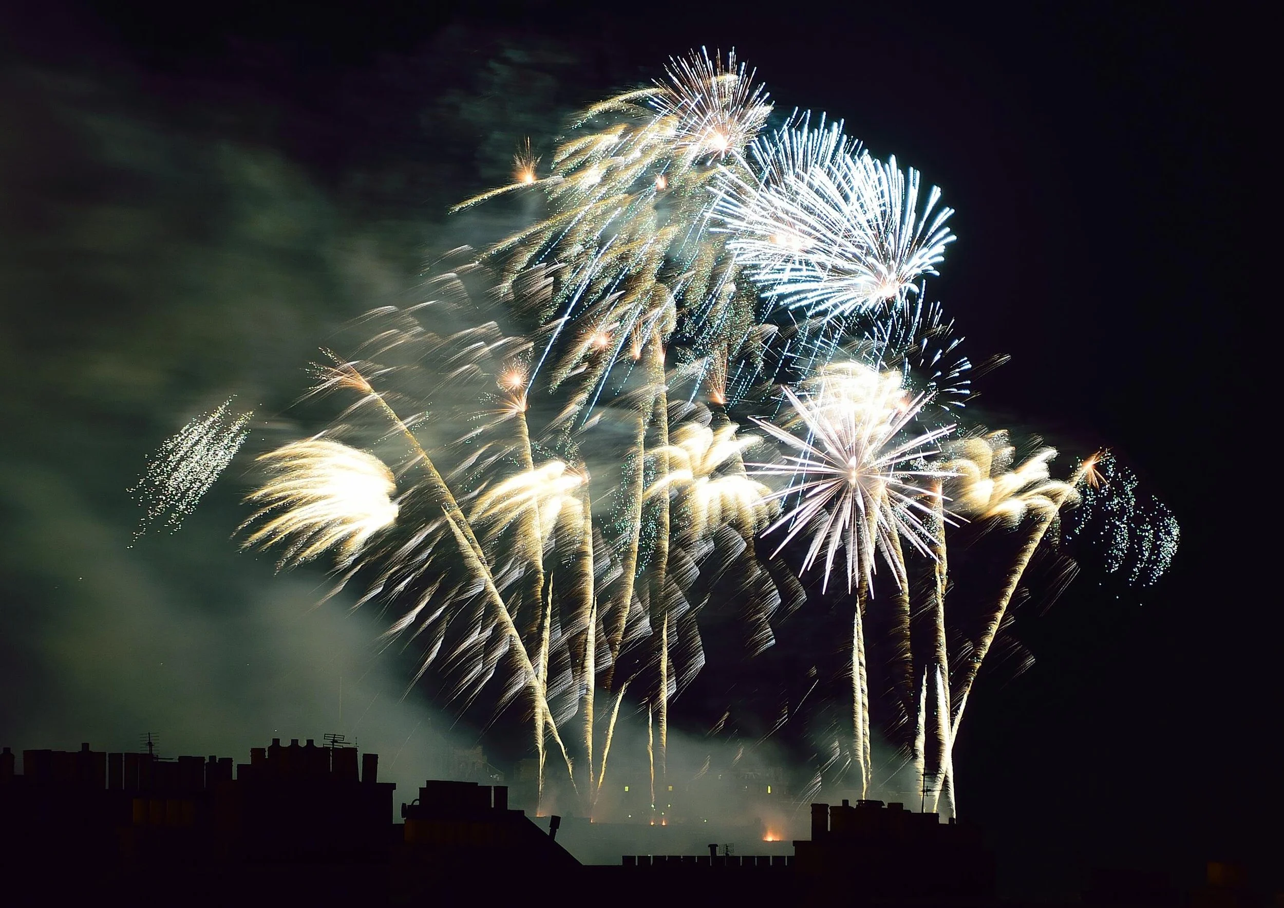 Colorful fireworks exploding in the night sky over silhouetted rooftops.