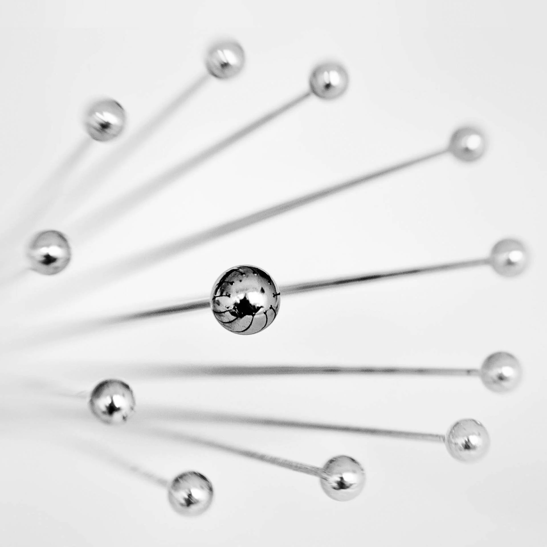 Close-up of metallic pins with spherical heads arranged in a fan shape.
