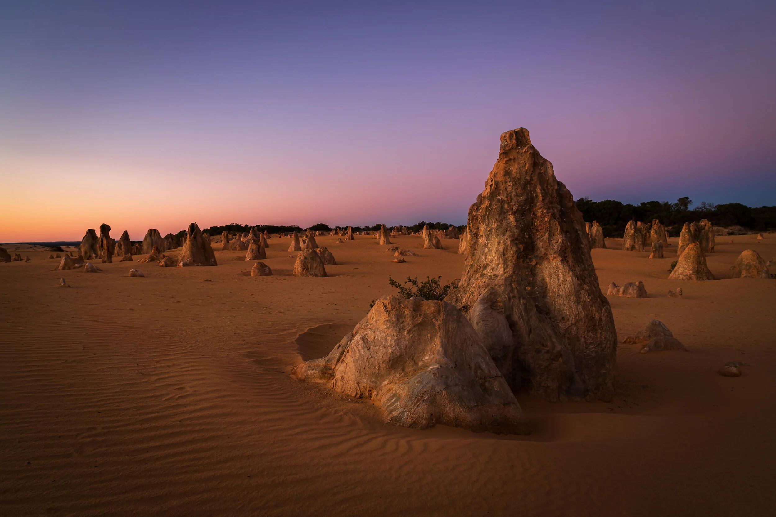 The Pinnacles Desert at sunset in Nambung National Park, Western Australia, featuring limestone formations and a colorful sky.