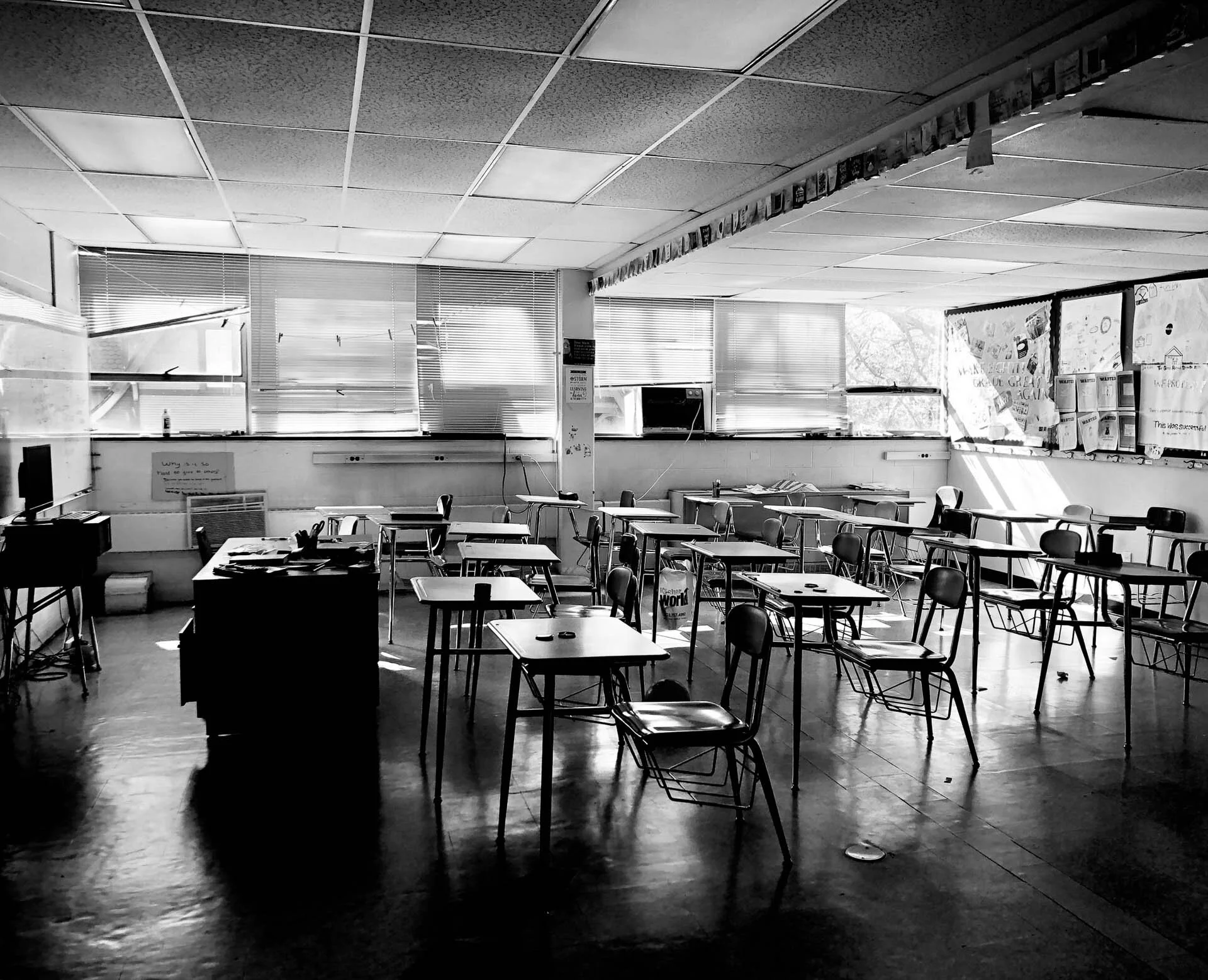 Black and white image of an empty classroom with desks, chairs, and decorations on the walls.